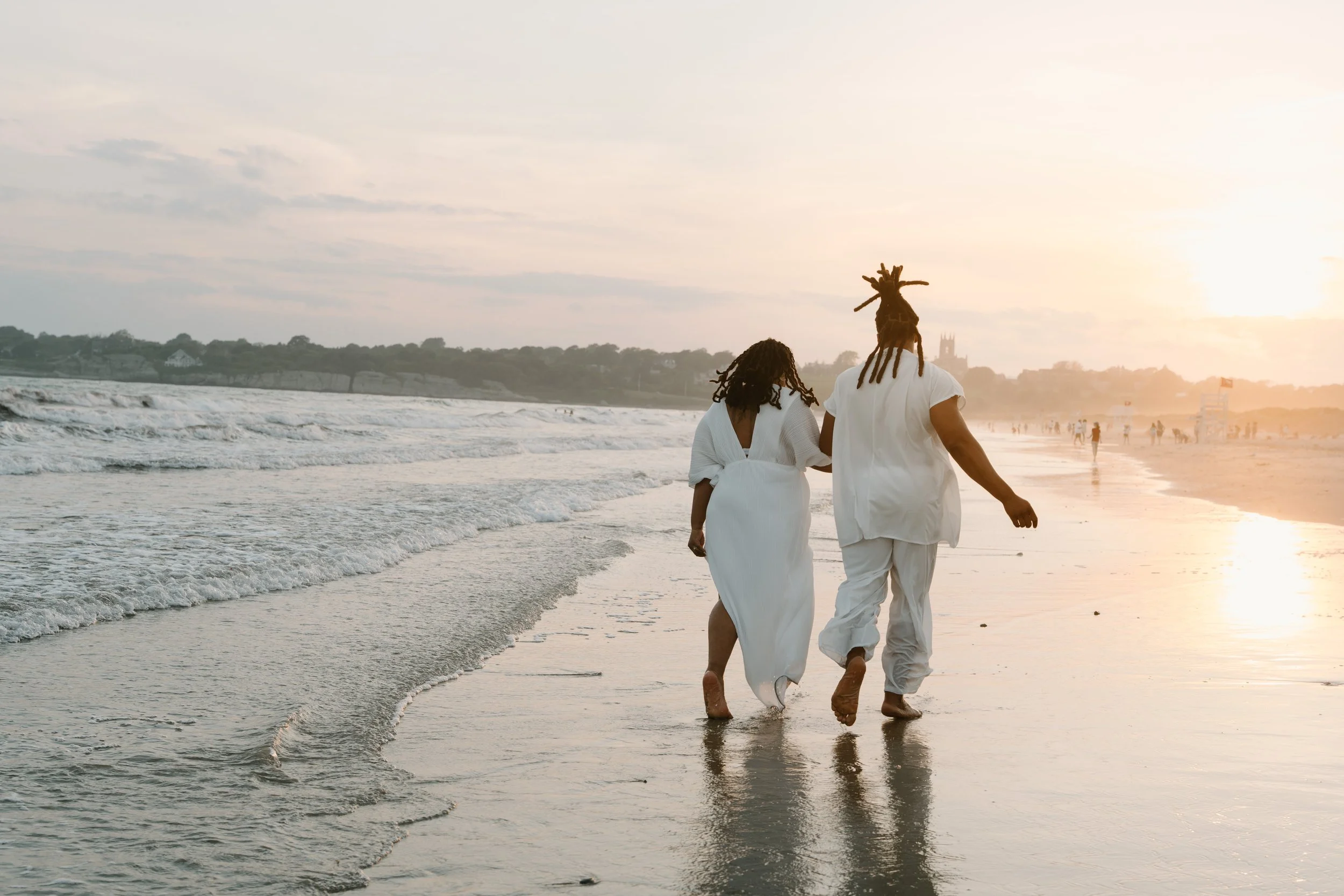 A couple walking on the beach at sunset, holding hands, with the ocean waves in the background at an elopement at Second Beach in Rhode Island. 