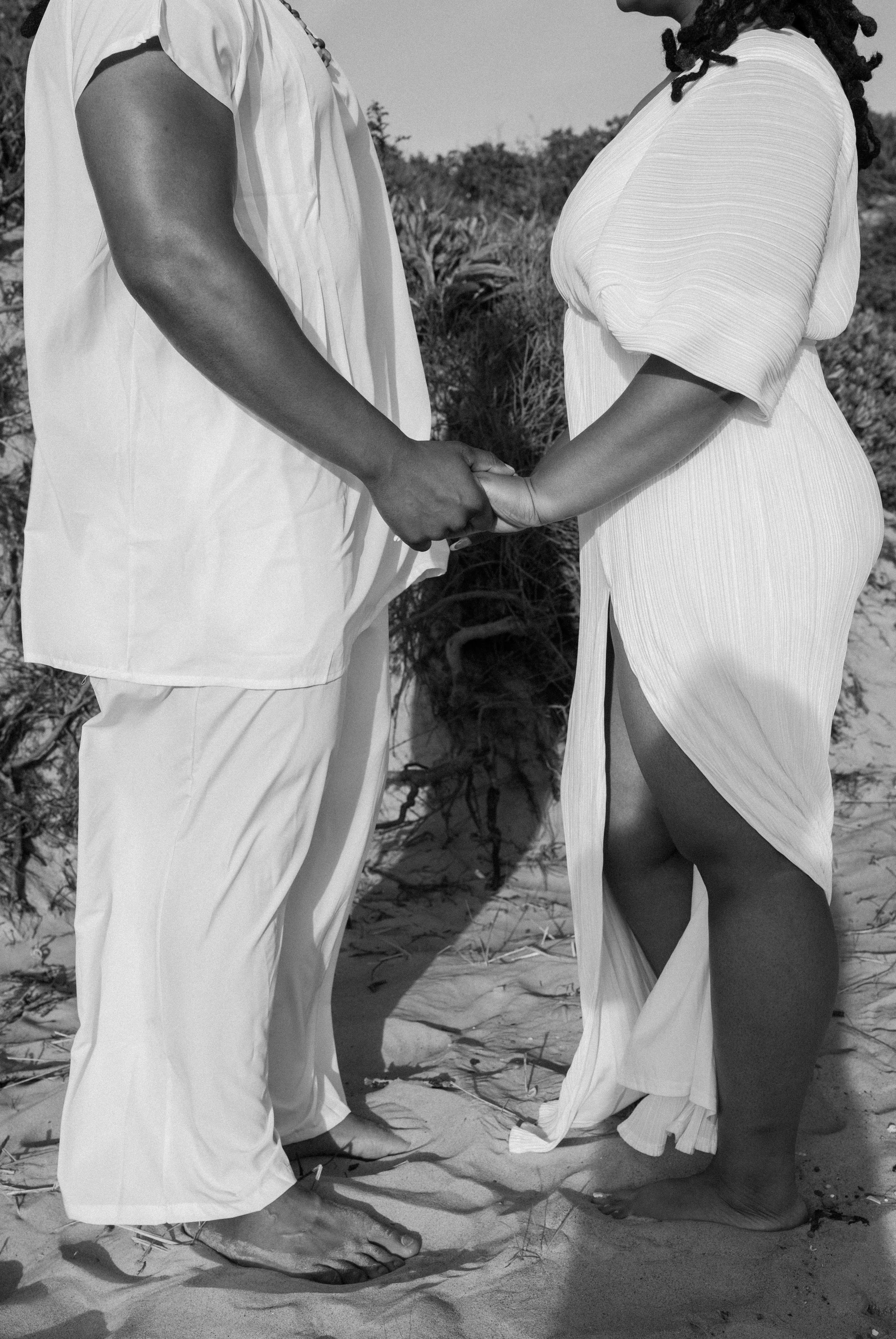 A couple holding hands on a sandy beach, wearing light-colored clothing, with tall grass in the background at an elopement at Second Beach in Rhode Island. 