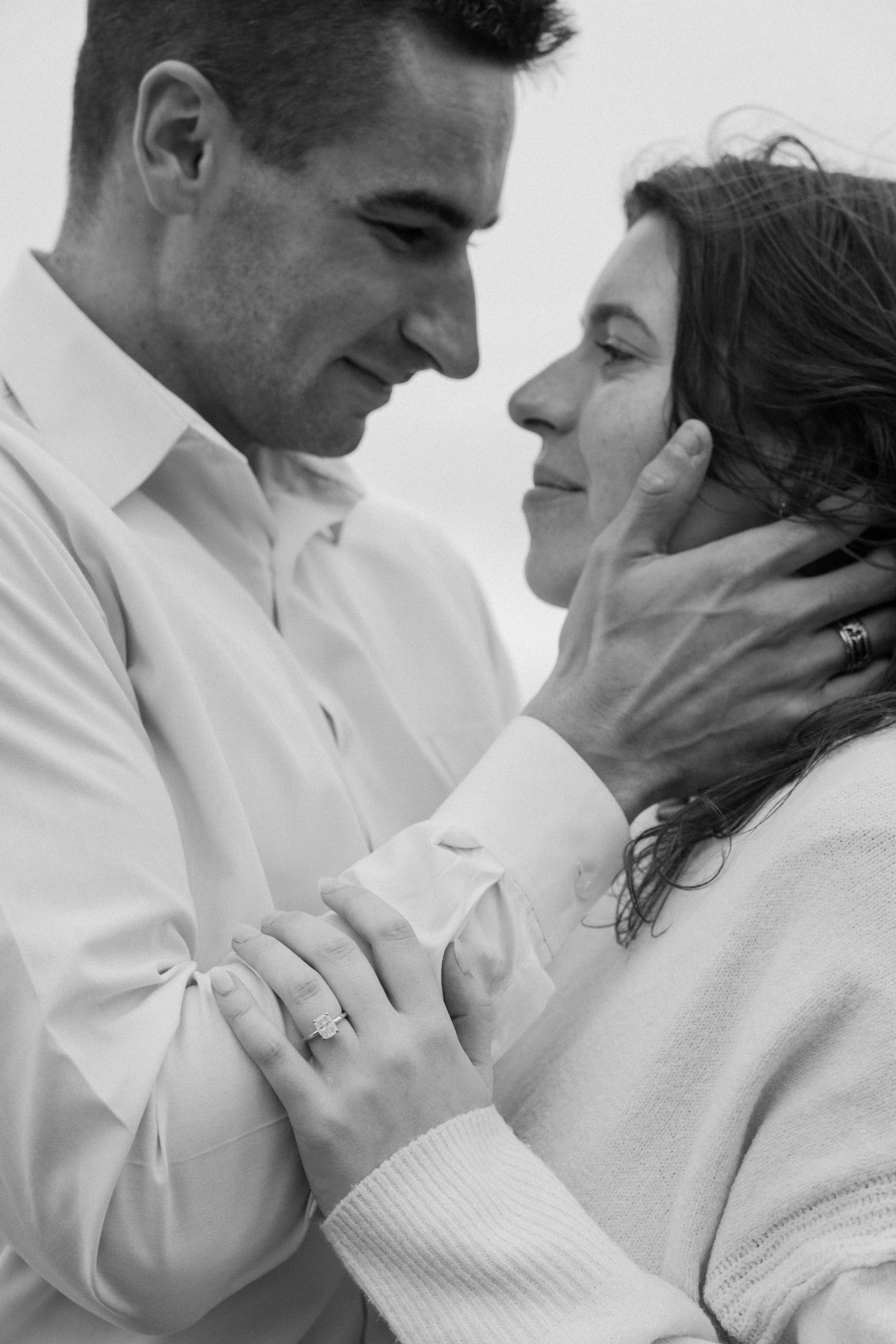 A man gently holds a woman's face with both hands, gazing into her eyes, showing an intimate and affectionate moment for an engagement photo session in Galway, Ireland. 