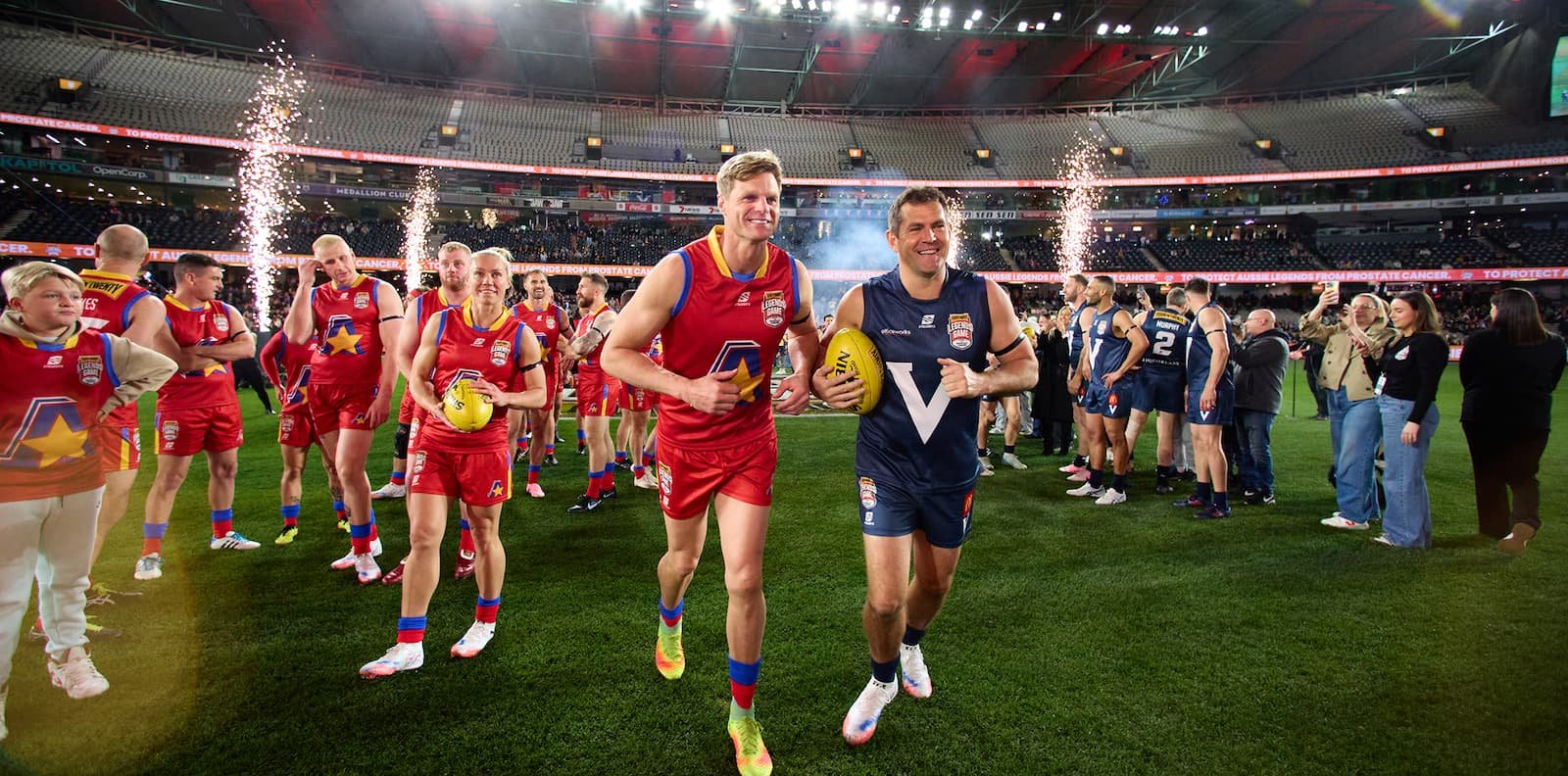 AFL players at the Legends Game with fireworks on field, showcasing community engagement and sport-led events managed by Prince Sports & Entertainment
