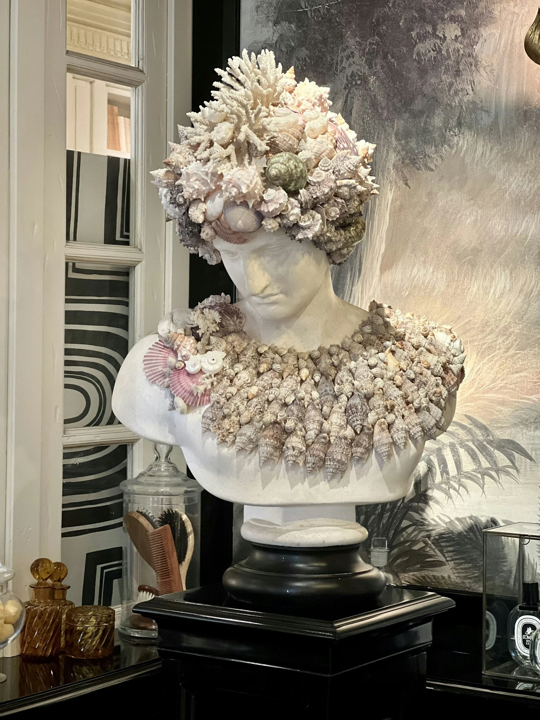 A bust sculpture decorated with seashells, coral, and sea life elements, resembling a woman with a headpiece made of various seashells and coral.