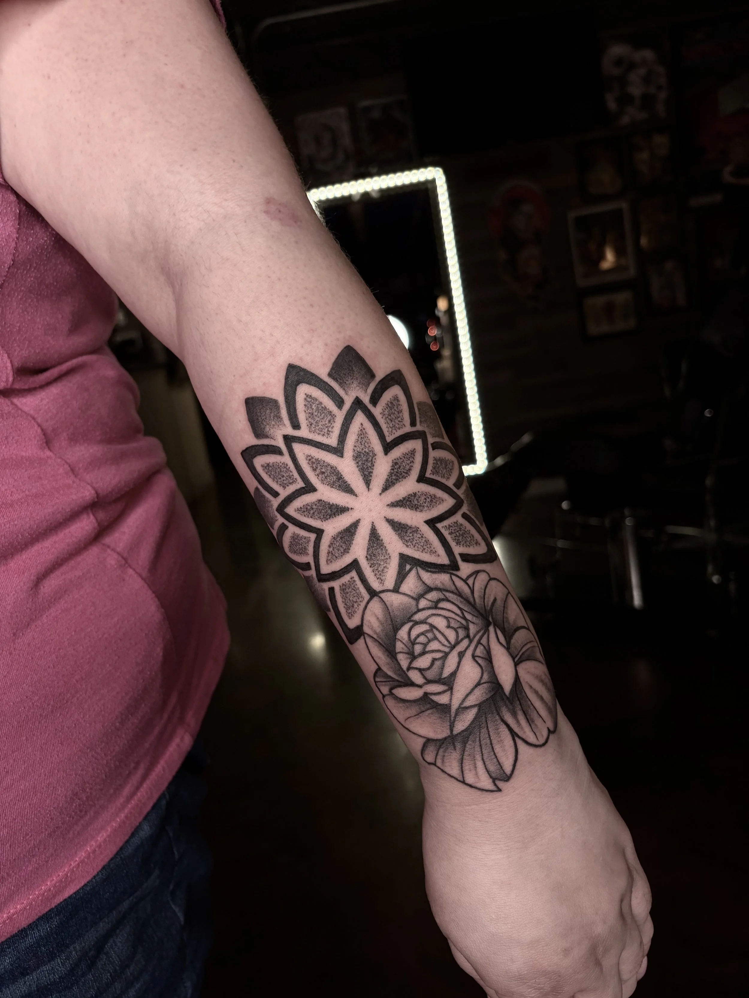 Tattoo of a geometric flower and a rose on a person's forearm.