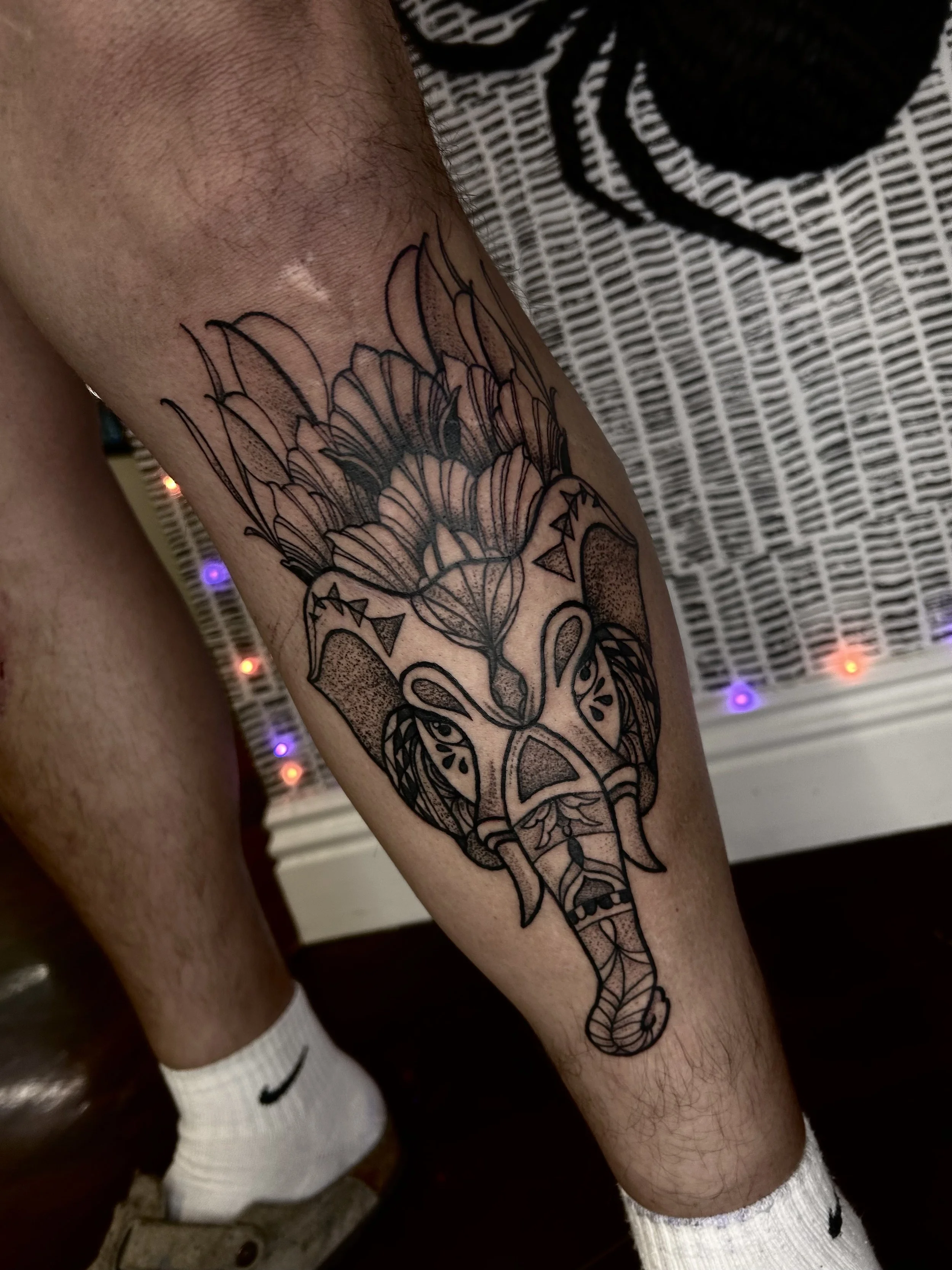 Line art tattoo of an animal, possibly a deer or elk, with a large flower and abstract geometric patterns on its head and body.
