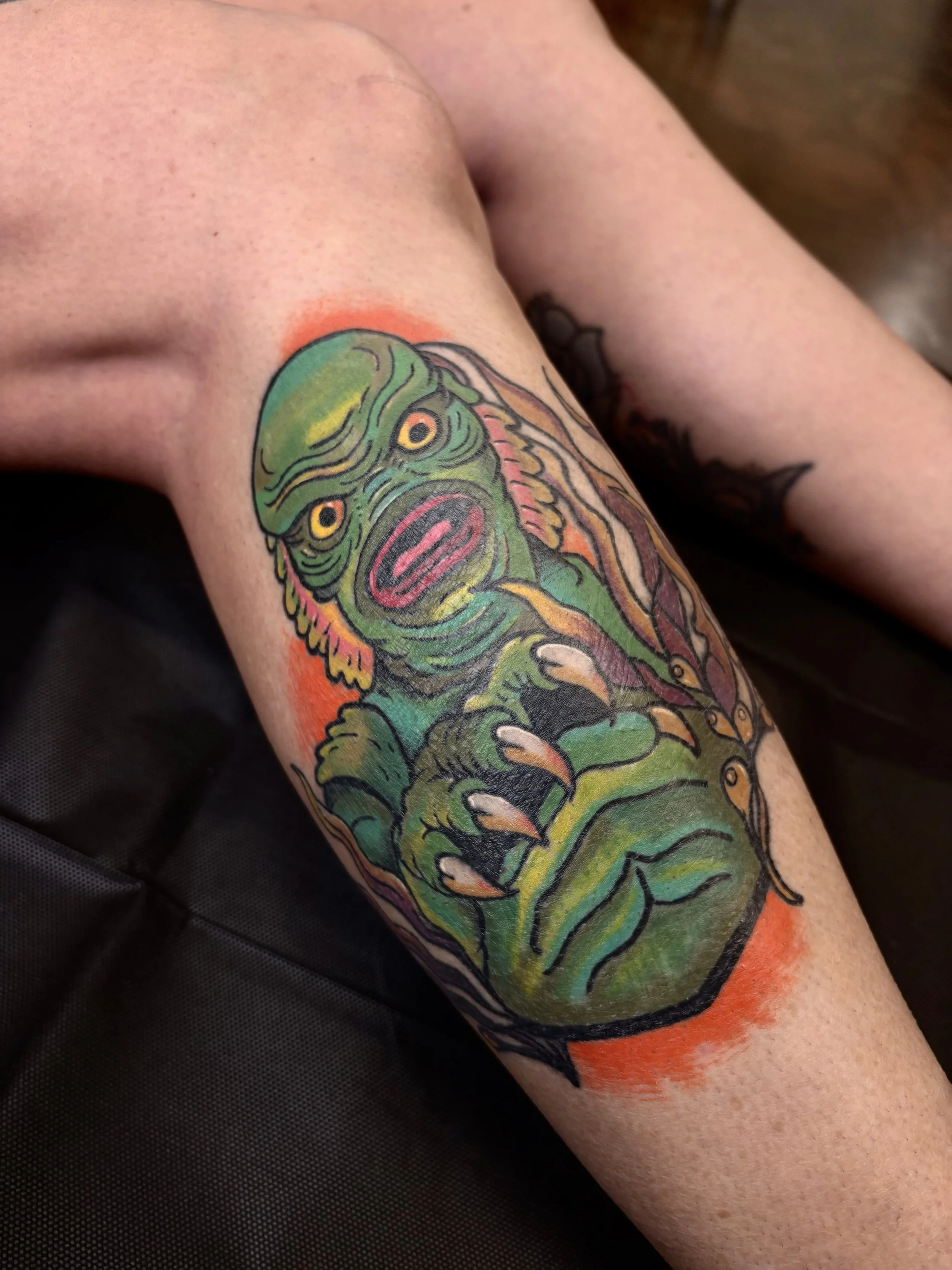 Colorful tattoo of a creature with a creature with a cat-like face, yellow eyes, sharp claws, and a dragon below it, on a person's arm.