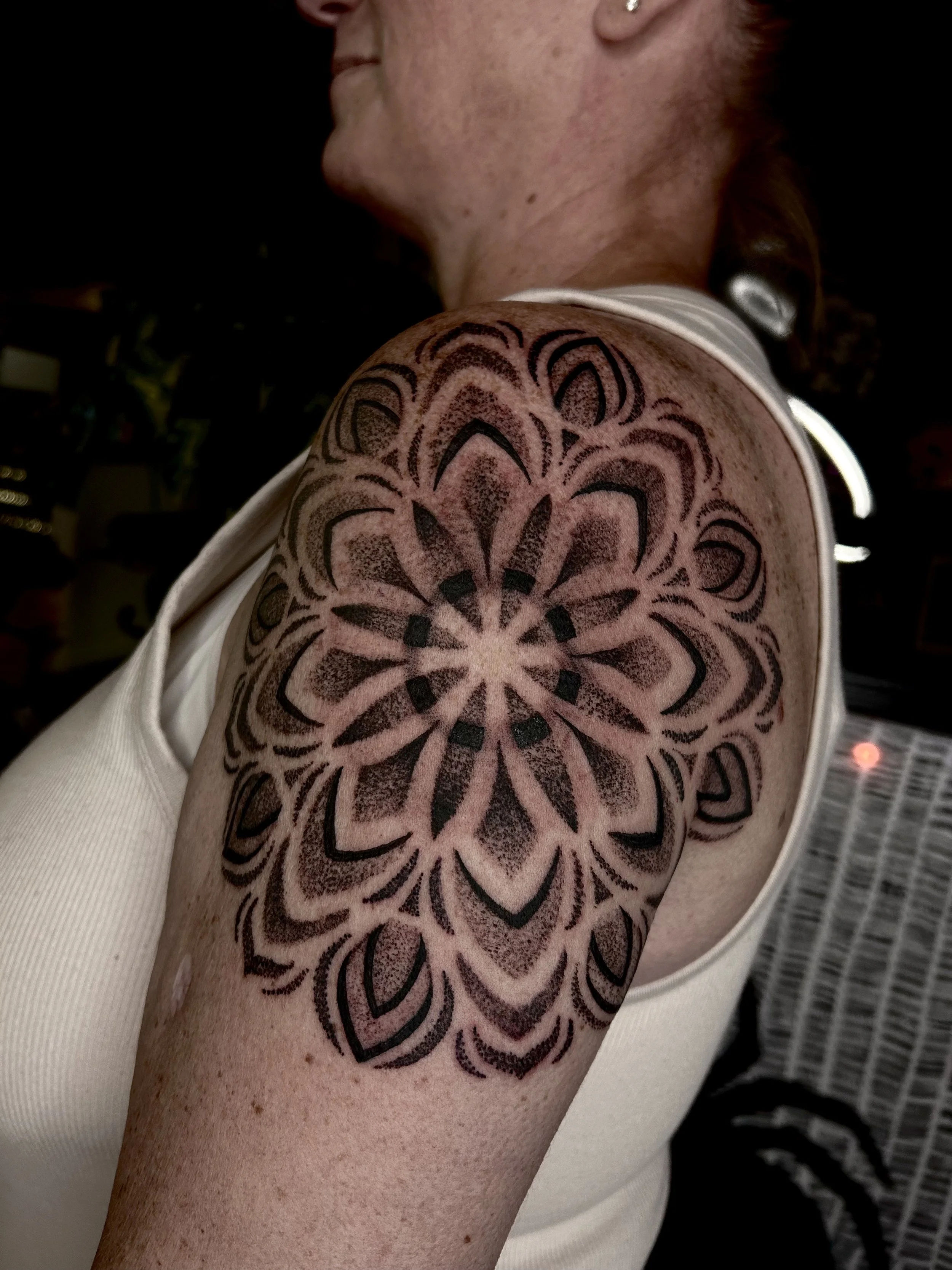 Black geometric floral tattoo on person's shoulder.