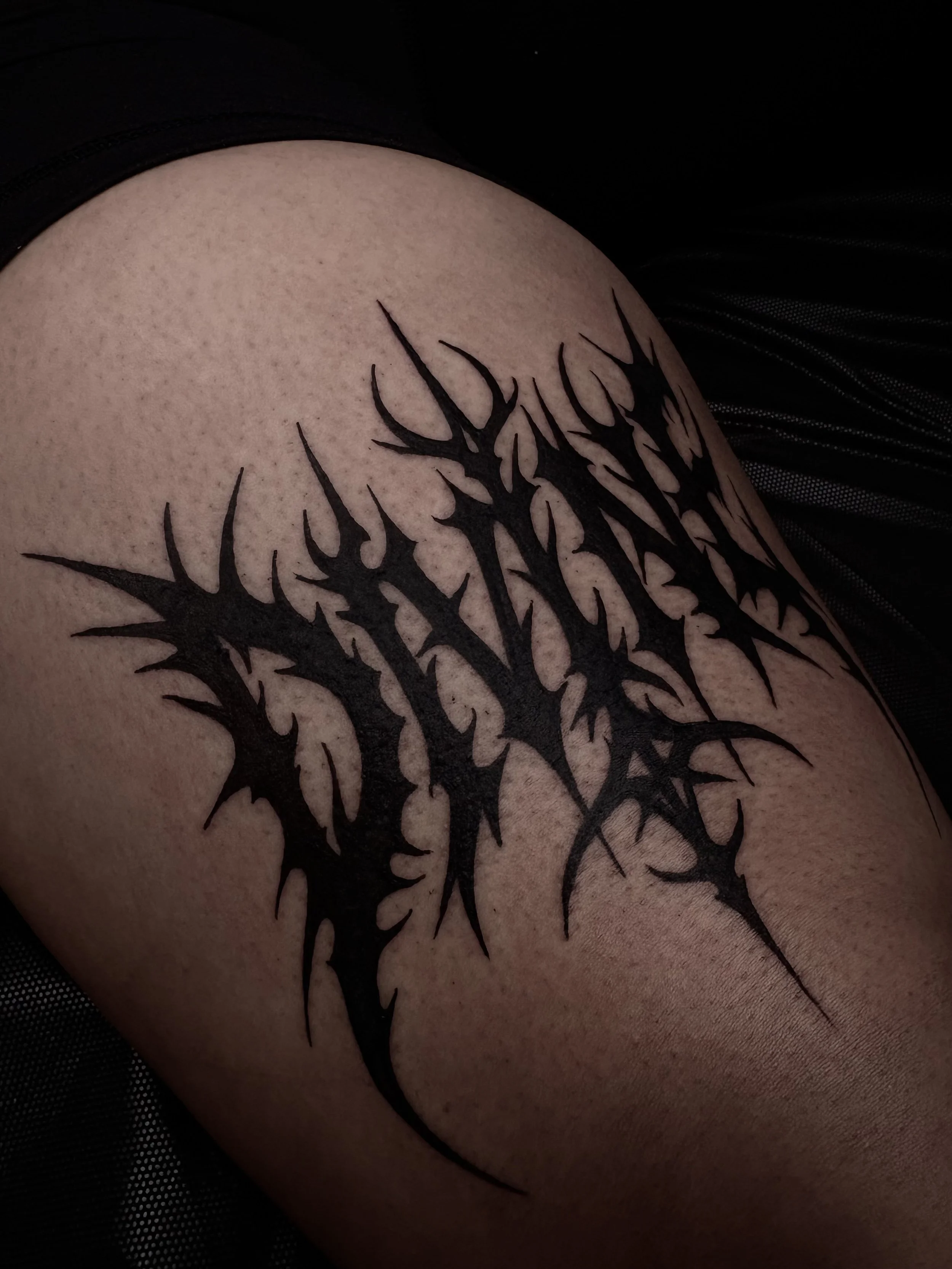 Black tribal-style tattoo on skin featuring jagged, spiky lines and sharp points.