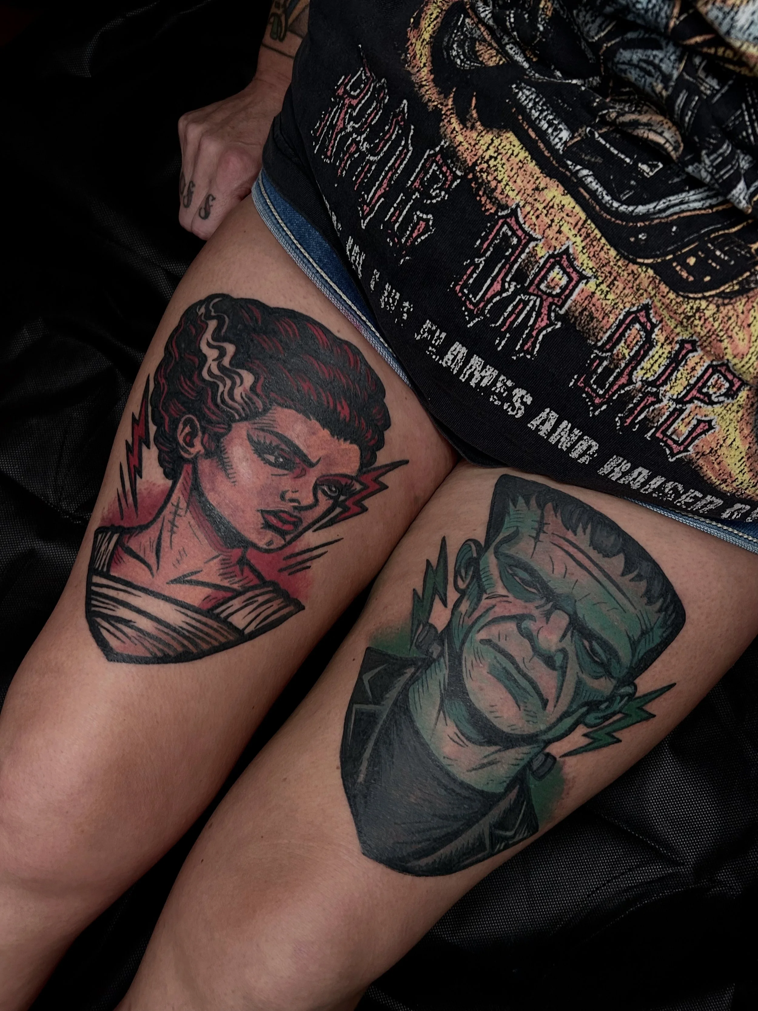 Tattoo of a woman with curly hair and a man with glasses, both with lightning bolt accents, on a person's thigh.