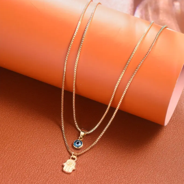 Embrace timeless protection and style with this Gold Plated Double Layer Evil Eye and Hamsa Hand Necklace from Mozzimo Jewelry.