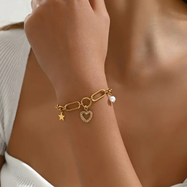 Drape your wrist in elegance with our Gold Plated Heart Charm Bracelet featuring pearls, stars, and chunky chain details.