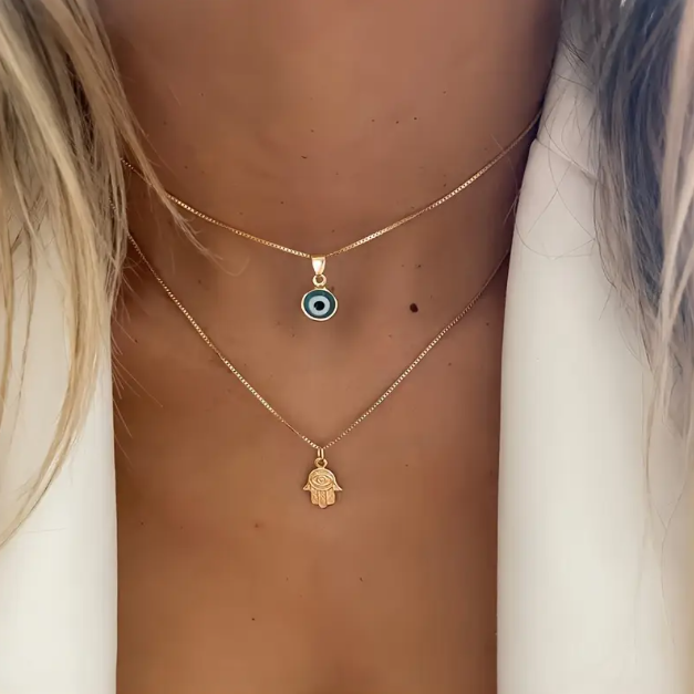 Embrace timeless protection and style with this Gold Plated Double Layer Evil Eye and Hamsa Hand Necklace from Mozzimo Jewelry.