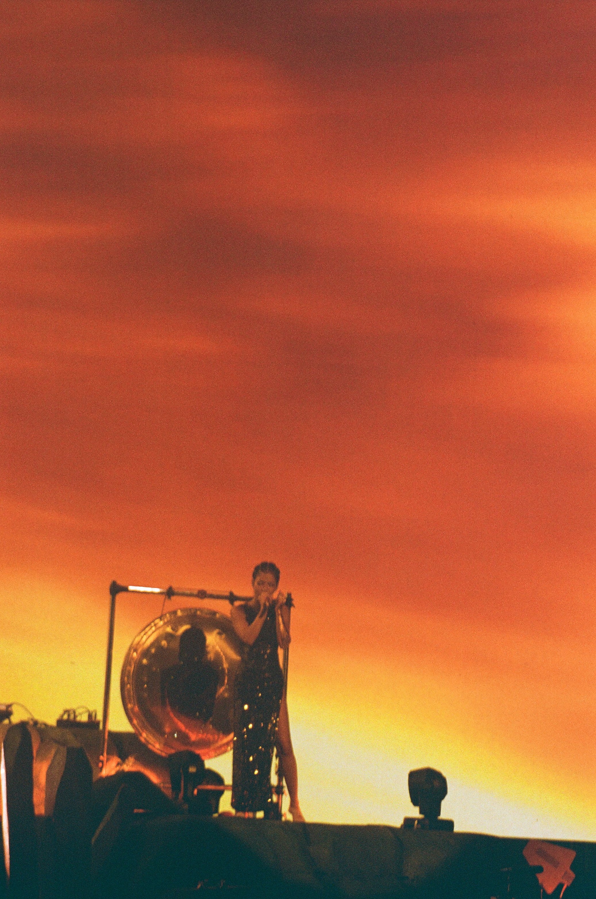 A woman in a sparkly dress singing into a microphone on a stage with a large gong and stage lights.