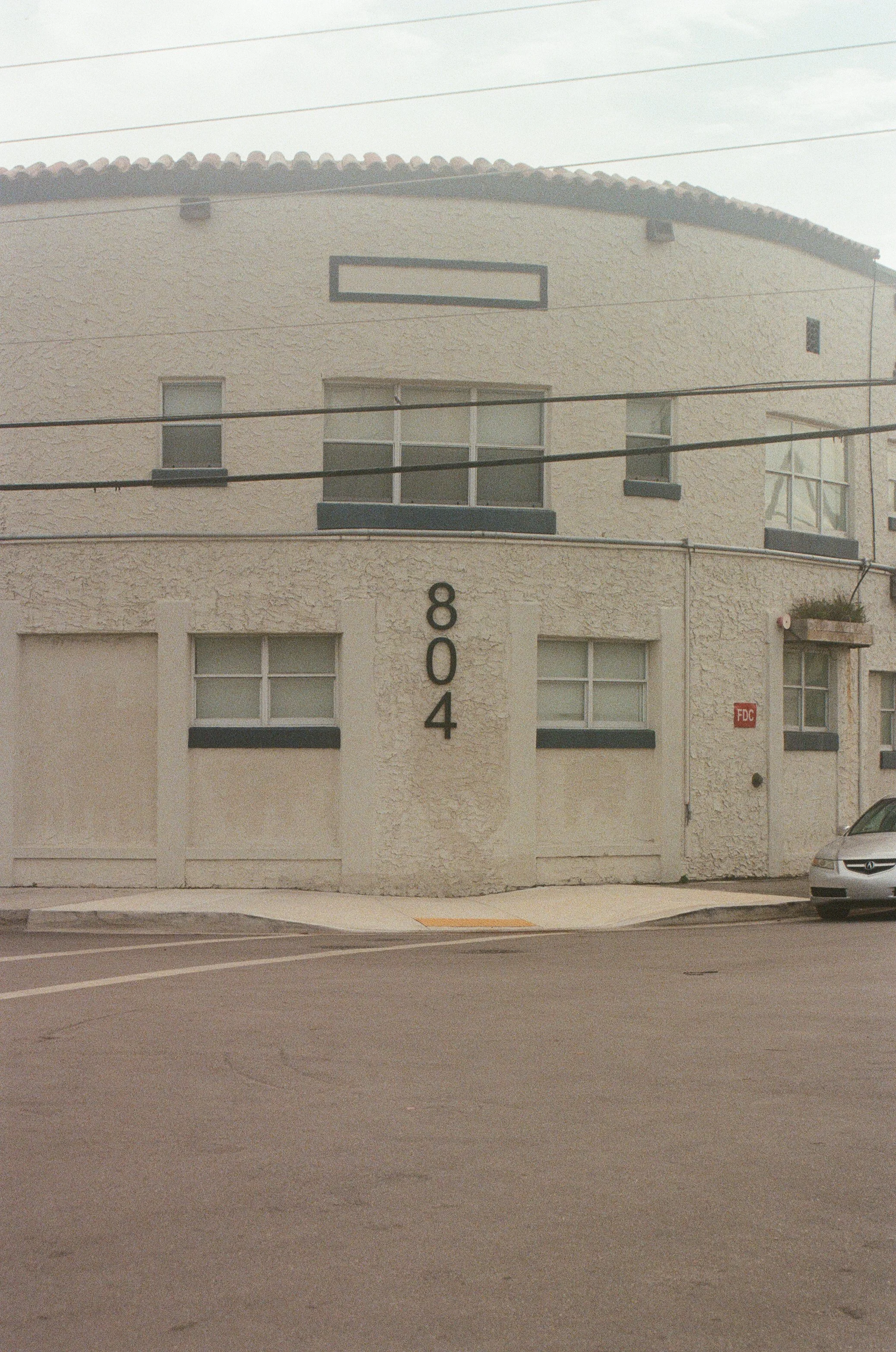 A beige building with dark trim, displaying the address 804 and several windows. A silver car is partially visible on the right side, and there are power lines overhead.