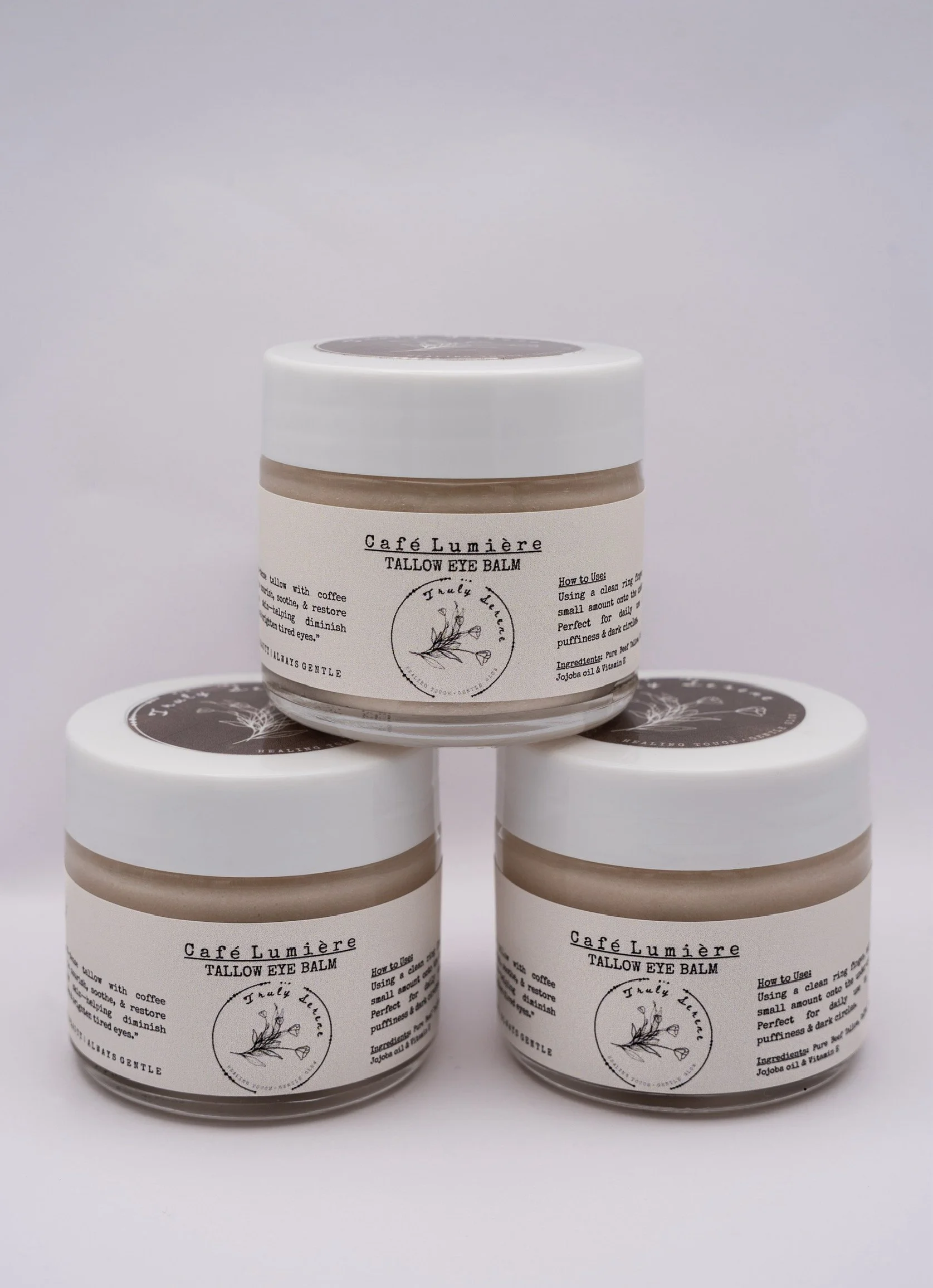 Three jars of Café Lumière Tallow Eye Balm stacked in a pyramid, with a plain white background.