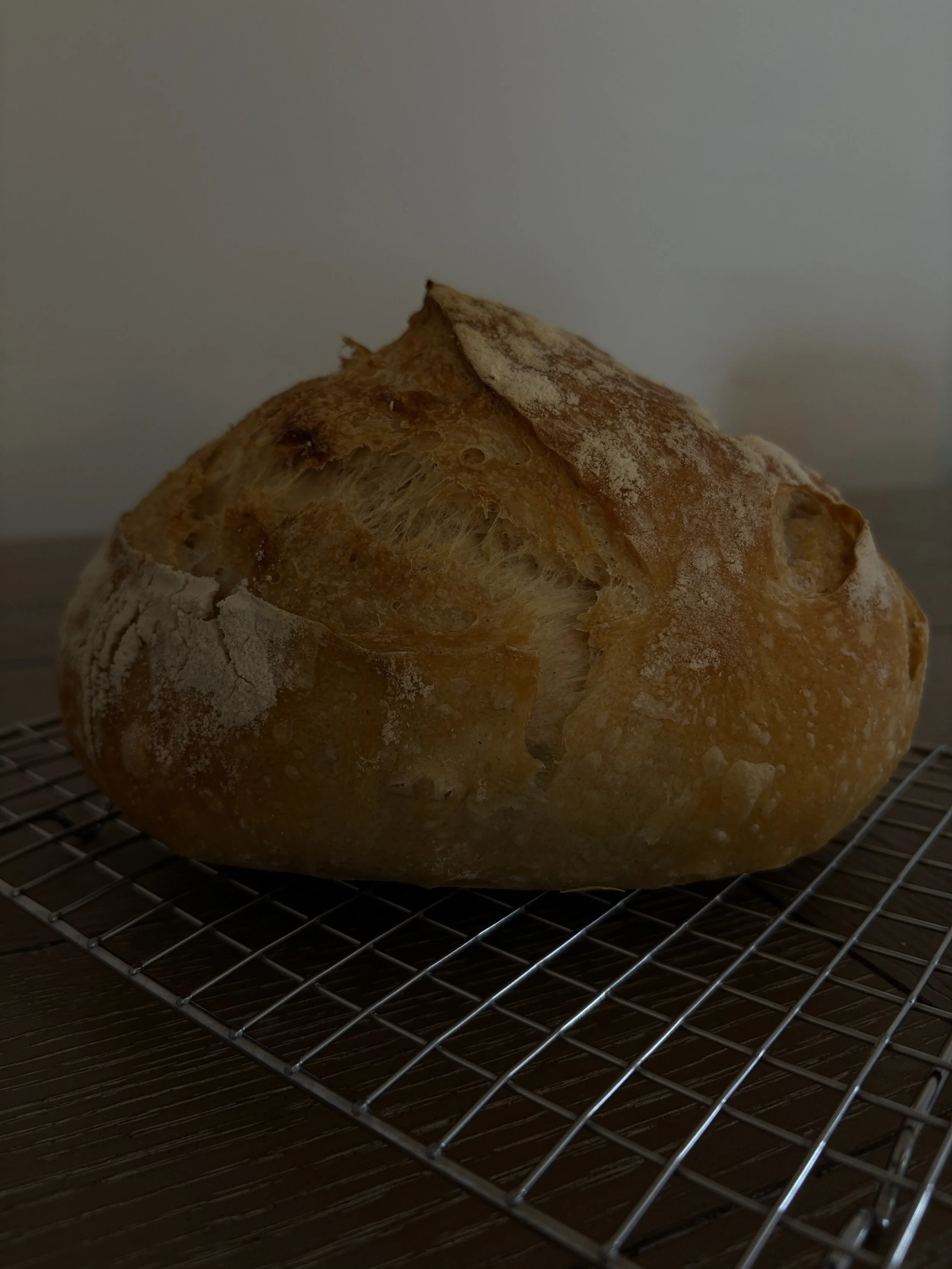 Close-up of a rustic loaf of bread with a crack on top, resting on a wire cooling rack.