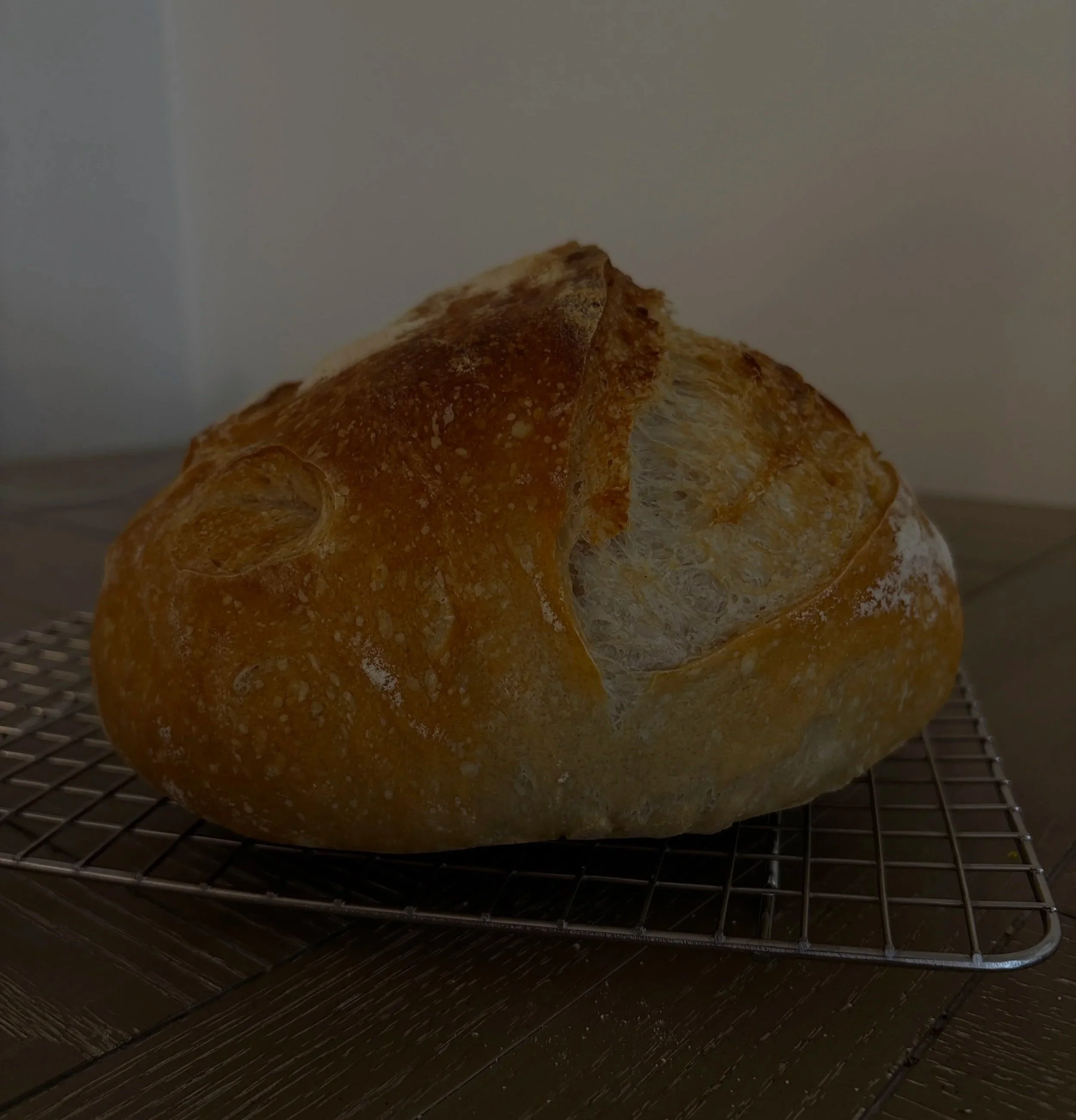 Close-up of a golden-brown baked bread loaf on a cooling rack inside a kitchen.