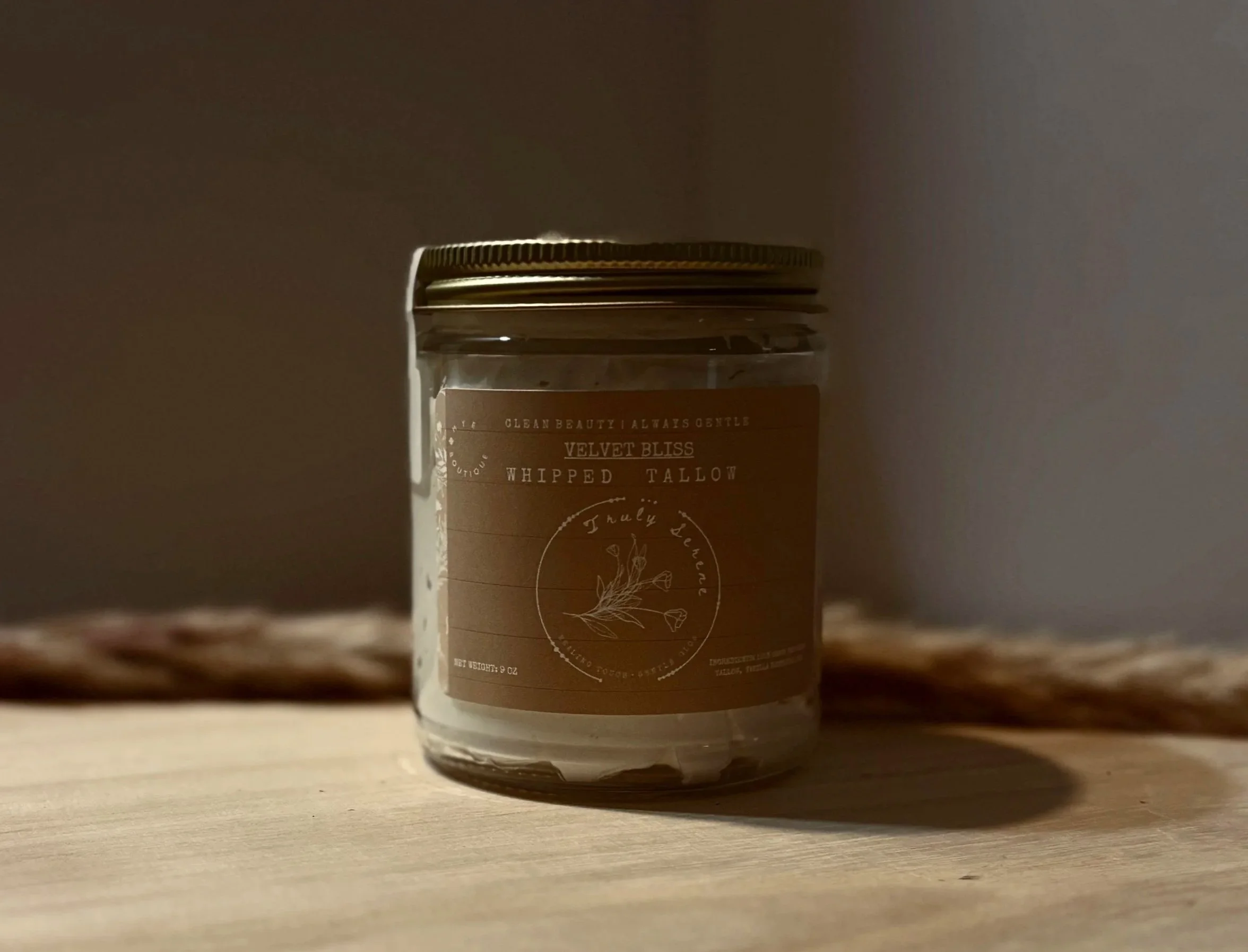 A small jar with a brown label containing product information, sitting on a wooden surface with a plain background.