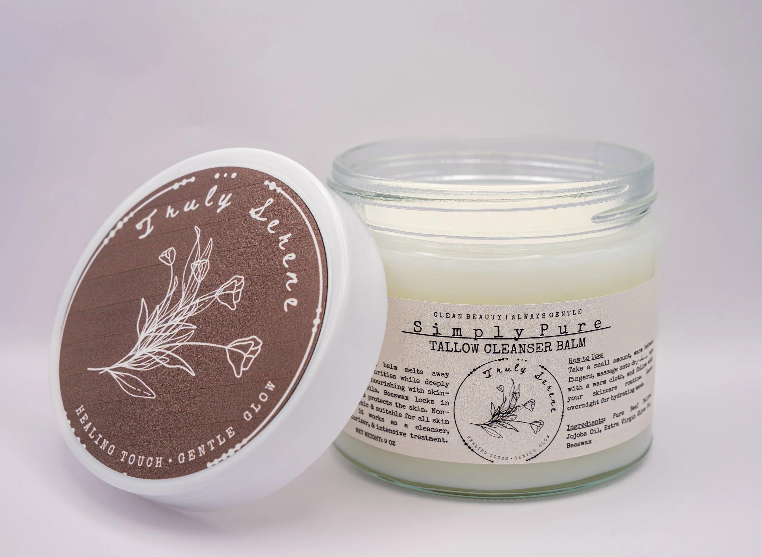 A jar of Simply Pure Tallow Cleanser Balm with the lid leaning against it, displaying a brown label with a white line drawing of a plant and the text 'July Tea' and 'Healing Touch - Gentle Glow'.
