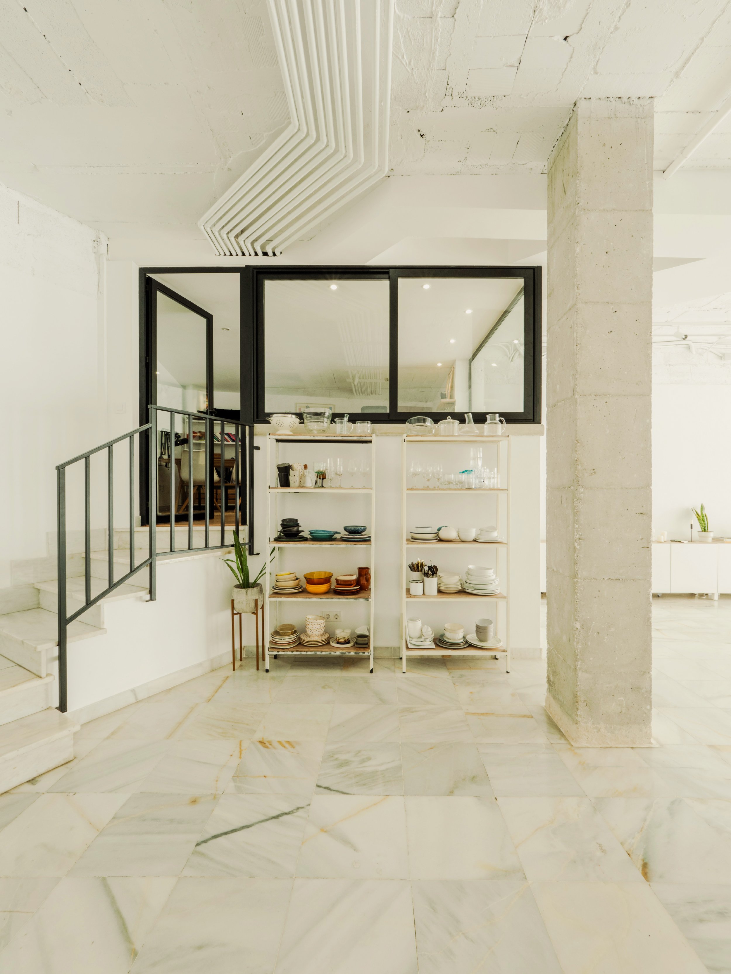 Espacio expositor con menaje de HOSPITALITY by Álvarez, escaleras a la sala privada insonorizada y columna de hormigón visto de estilo industrial mediterráneo. 