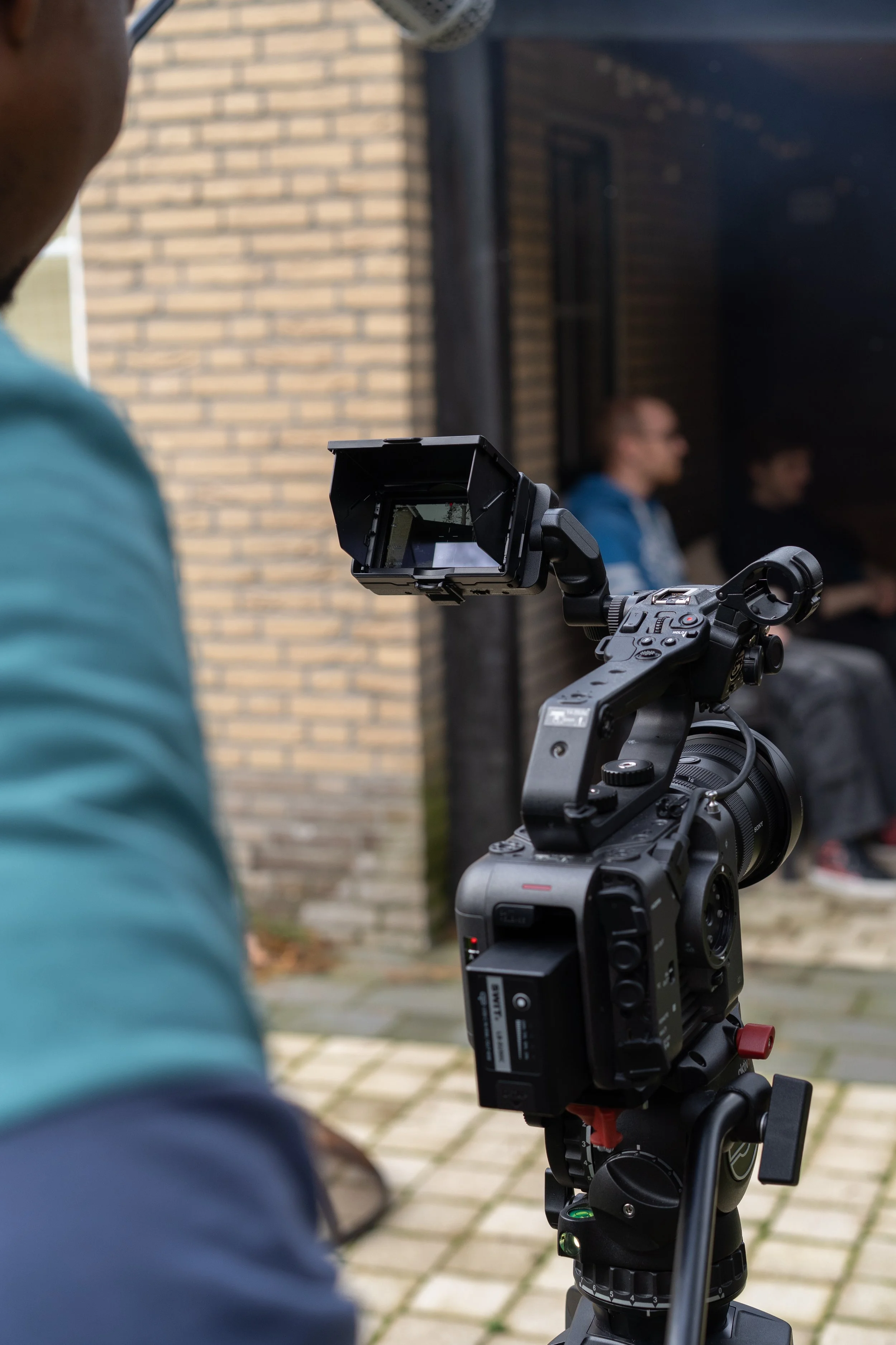 Cinematographer framing a wide shot on Sony FX6 during short film production with actors in the background