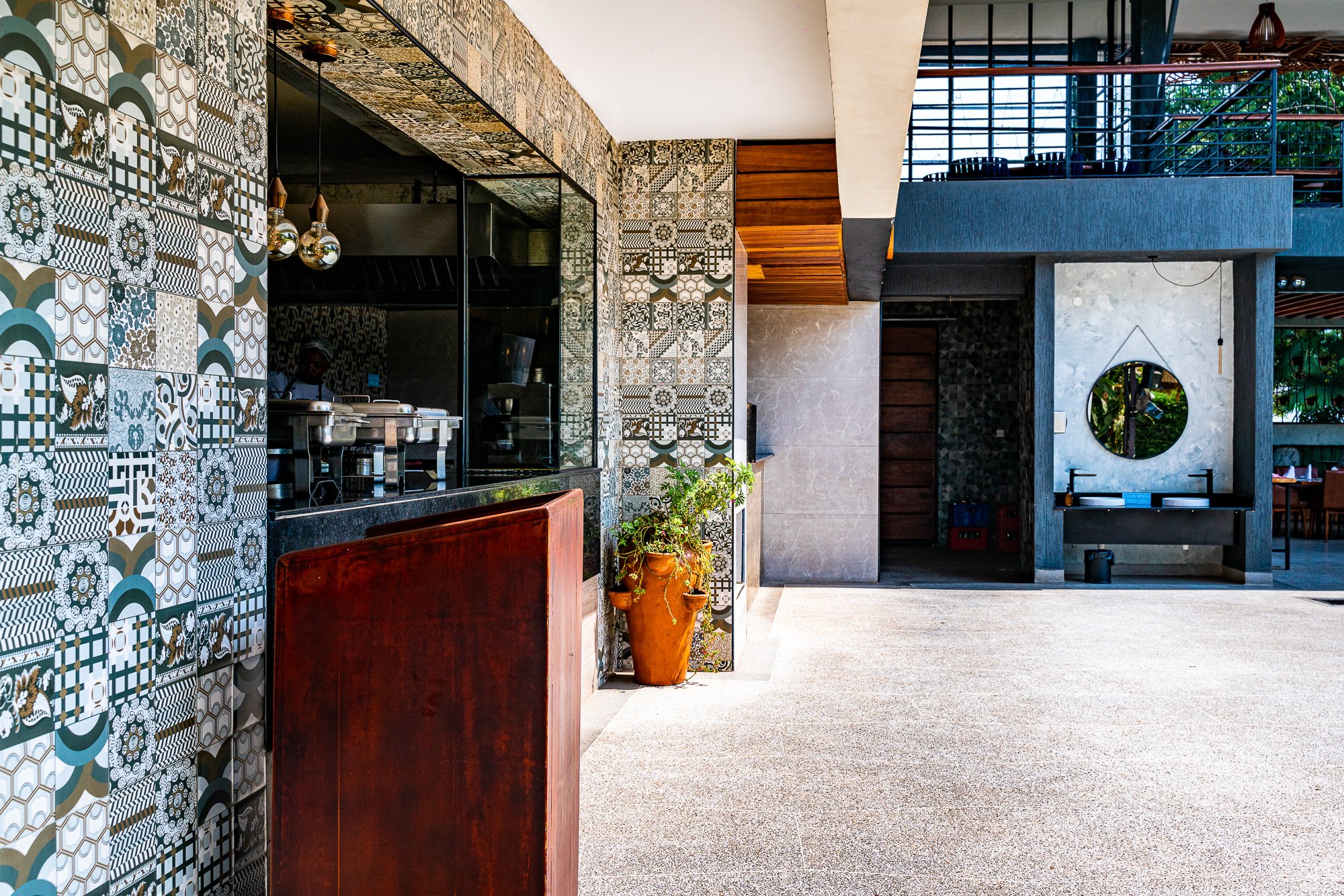 Modern outdoor area with patterned tile walls, a potted plant, and a mirror on a concrete wall.