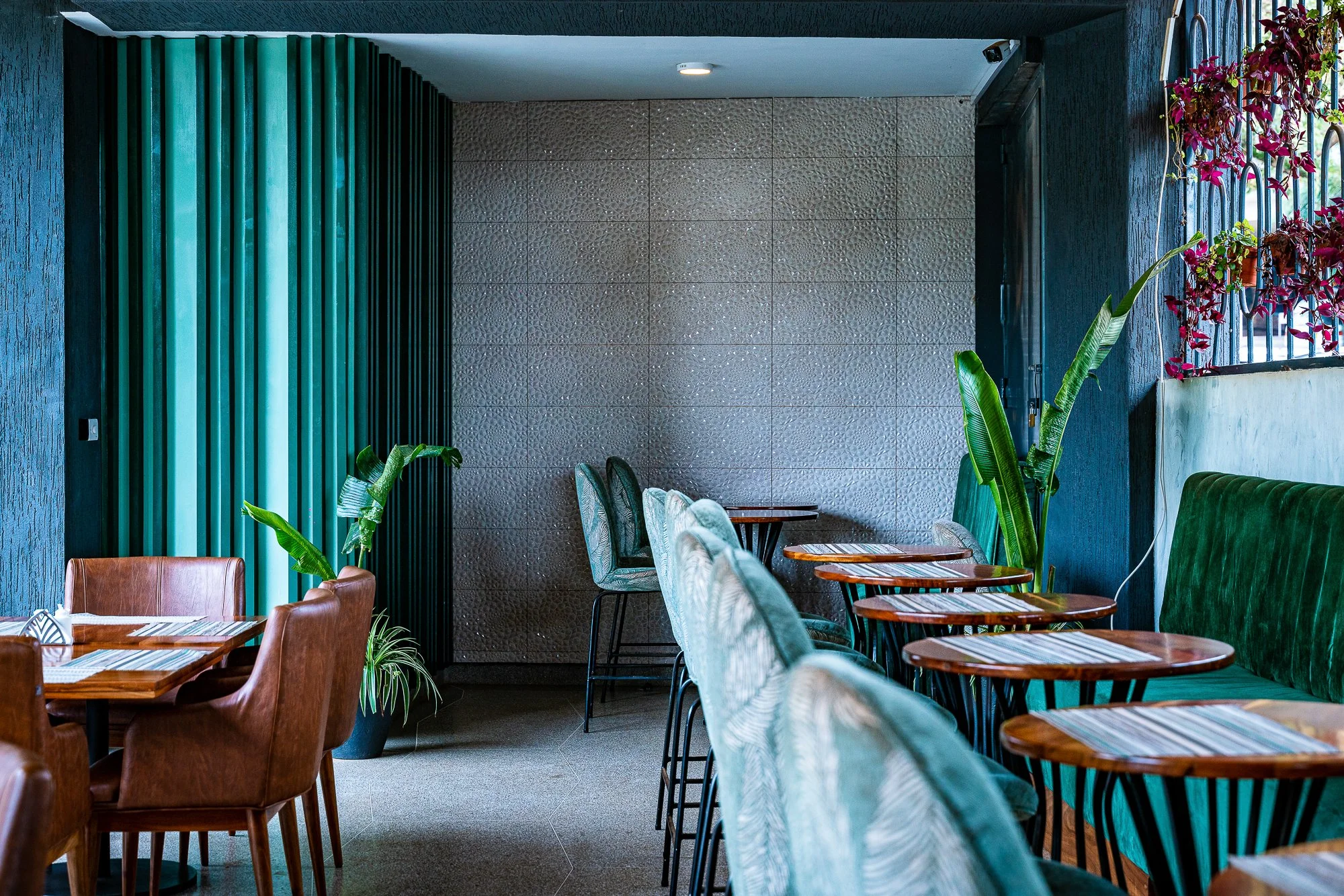 Interior of a restaurant with seating featuring green and brown chairs, wooden tables, potted plants, and decorative wall panels.