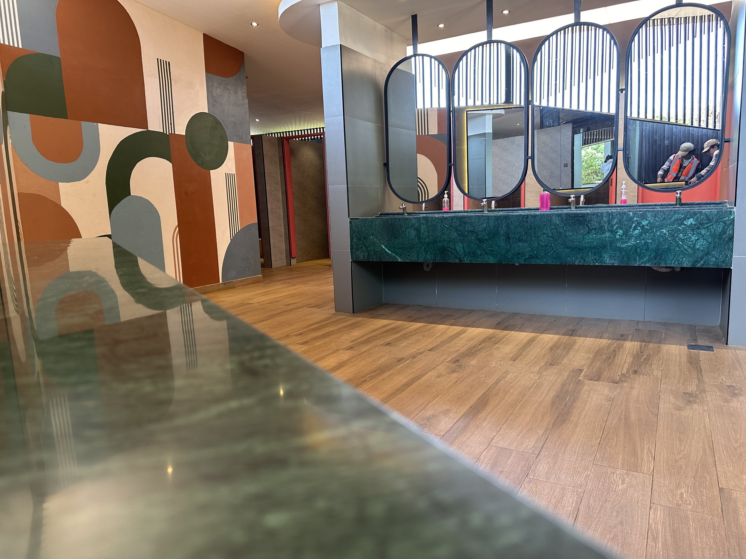 Interior of a modern restroom or wash area with a green marble counter and large vertical oval mirrors, and painted abstract mural on the wall.