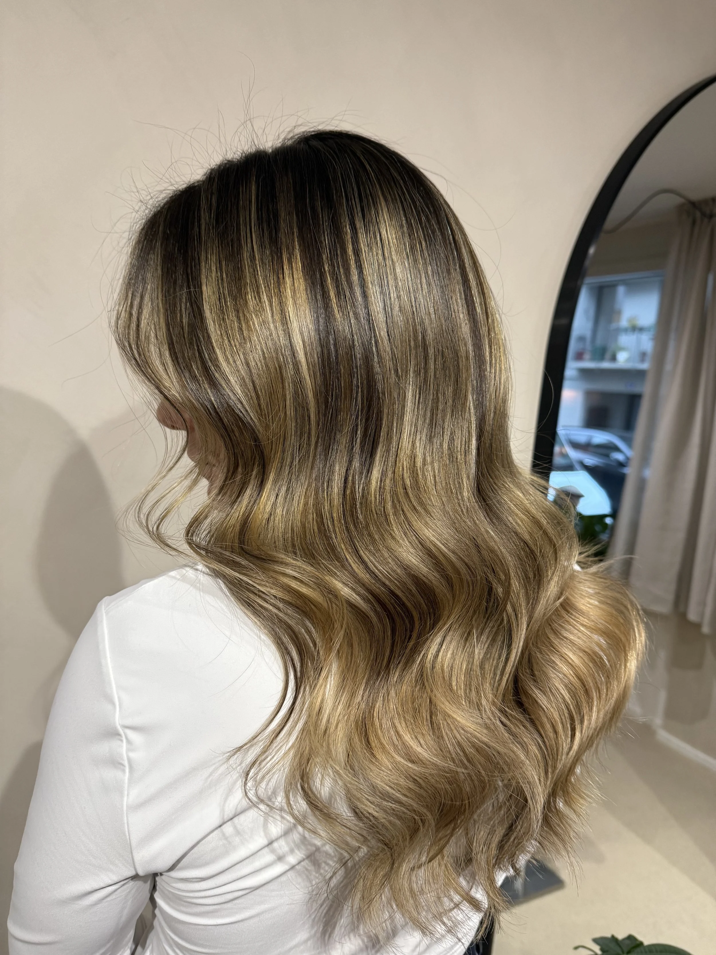 Woman with shoulder-length wavy hair featuring blonde highlights sitting in a salon or office environment.
