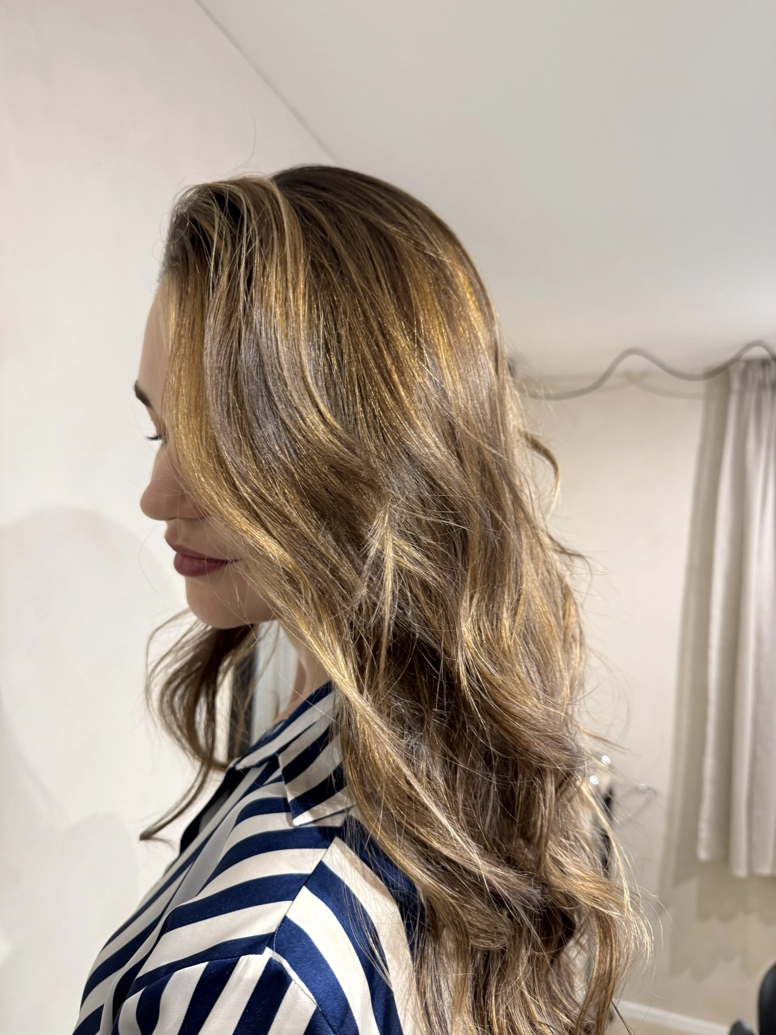 A woman with long, wavy, light brown hair sitting in a salon chair.