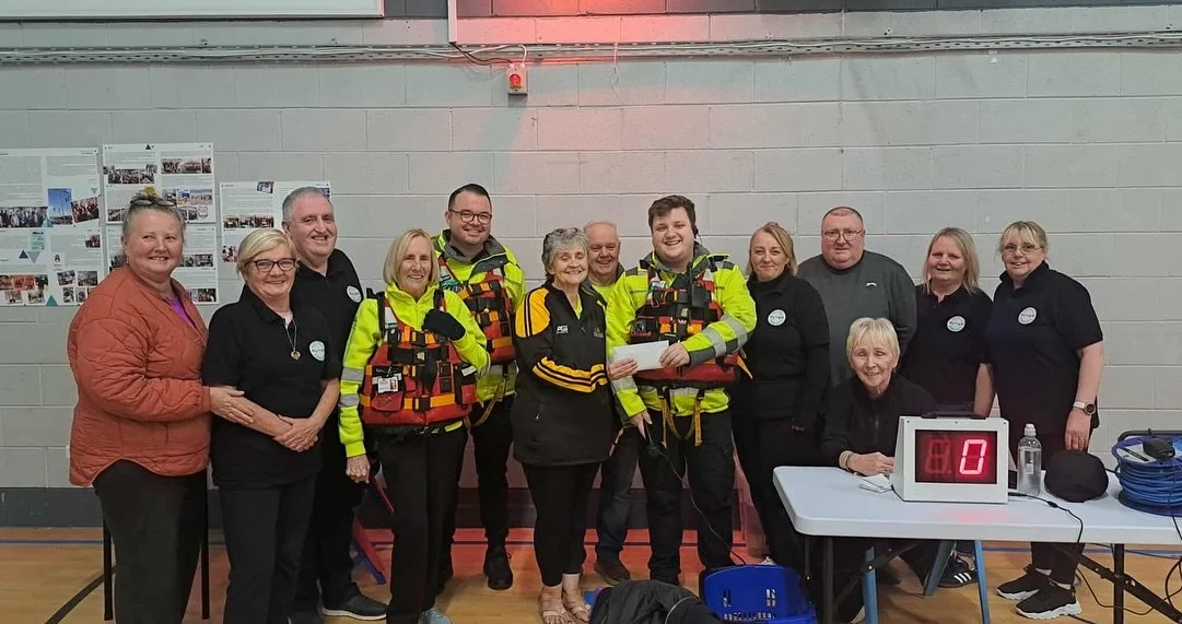 Group of people standing indoors, some wearing emergency response vests, fooling with a sign displaying the number zero