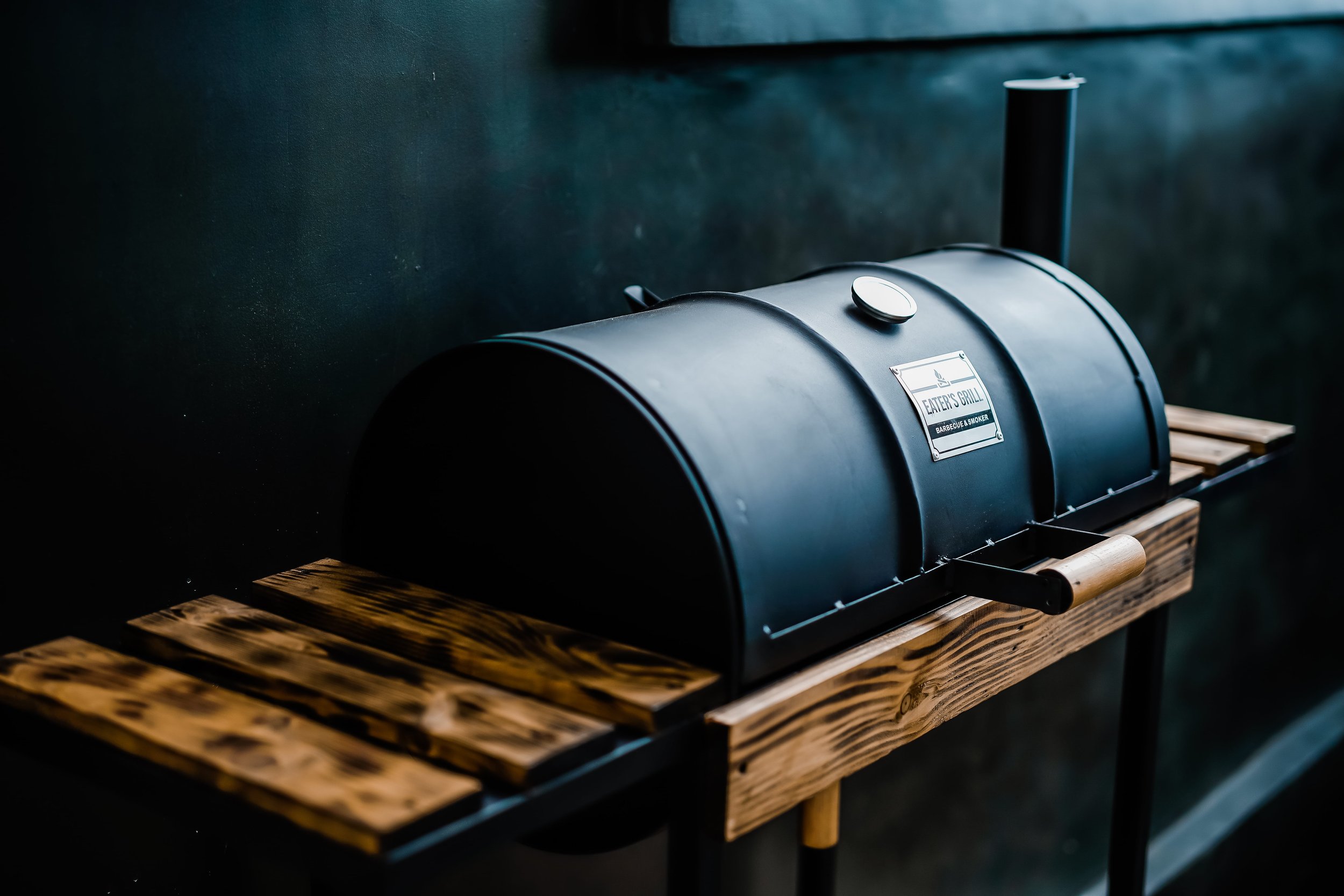 Black charcoal grill with wooden side shelves against a dark background