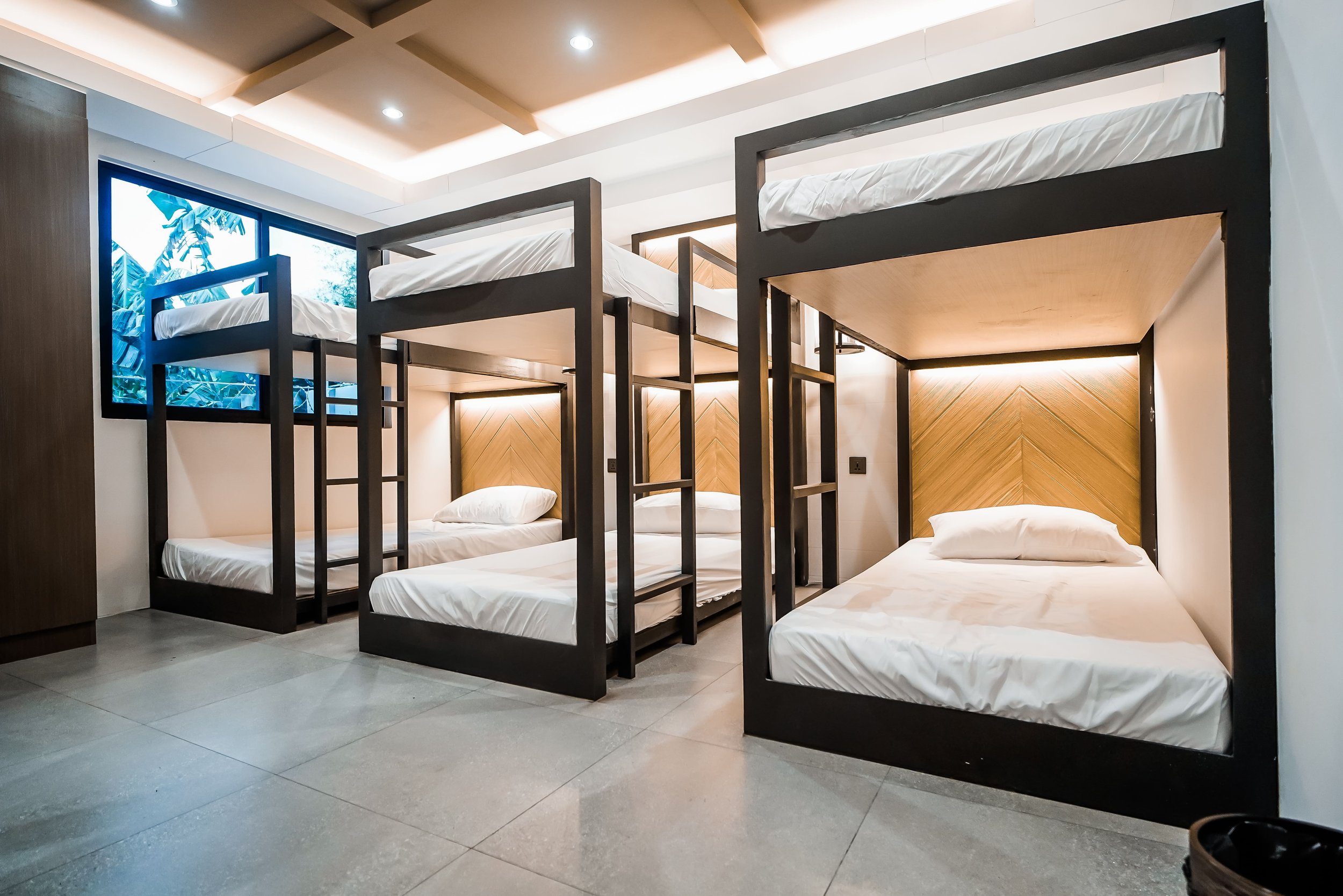 Modern dormitory room with triple bunk beds, white bedding, and wooden accents.