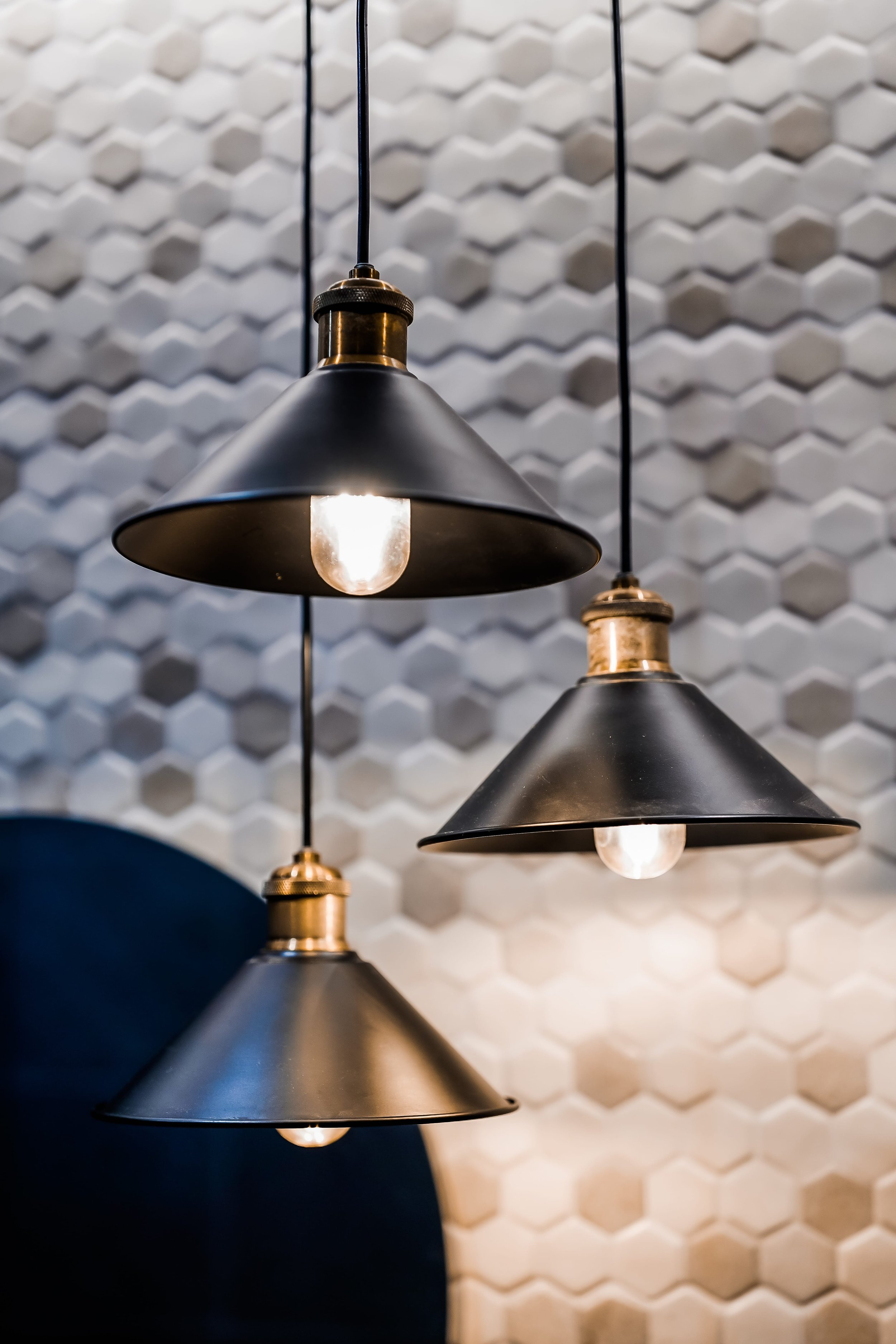 Three black pendant lights with exposed bulbs hanging in front of a hexagonal textured wall.