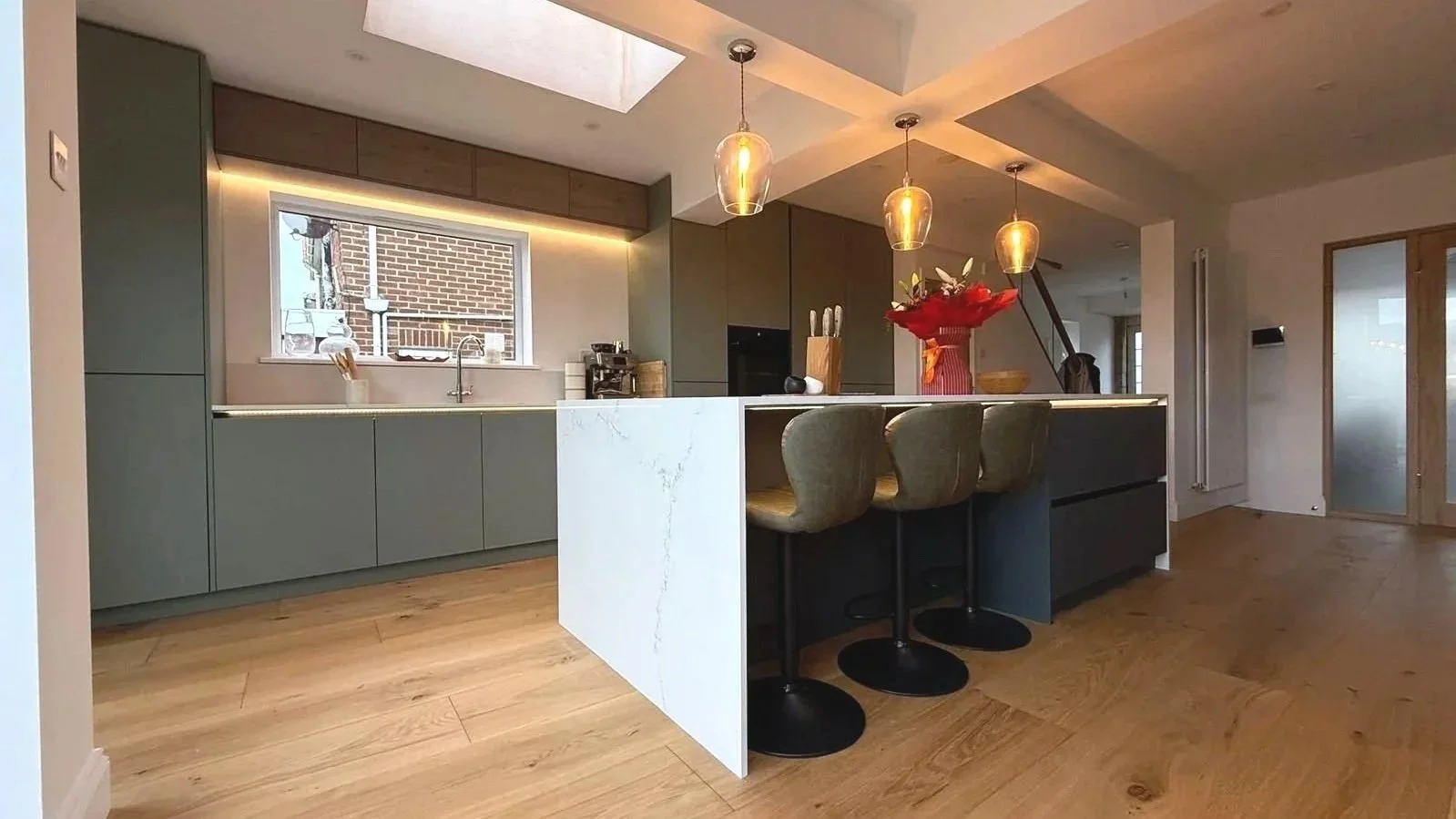 Modern kitchen with black marble island, built-in oven, white upper cabinets, black countertop, and bar seating with two chairs.