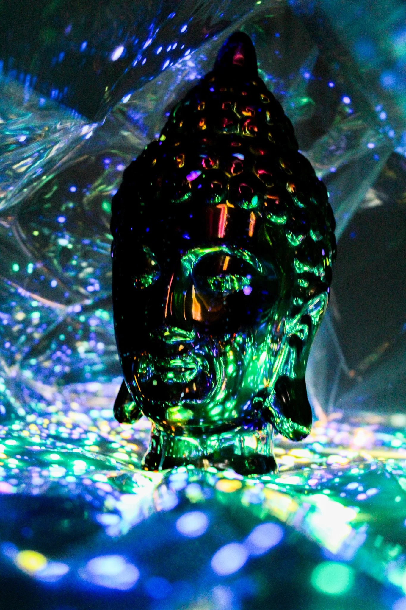 A black figurine of a person with a hat or hair is surrounded by colorful, glowing, holographic lights and reflections. The scene is surreal and abstract, with vibrant lights creating a cosmic or futuristic atmosphere.