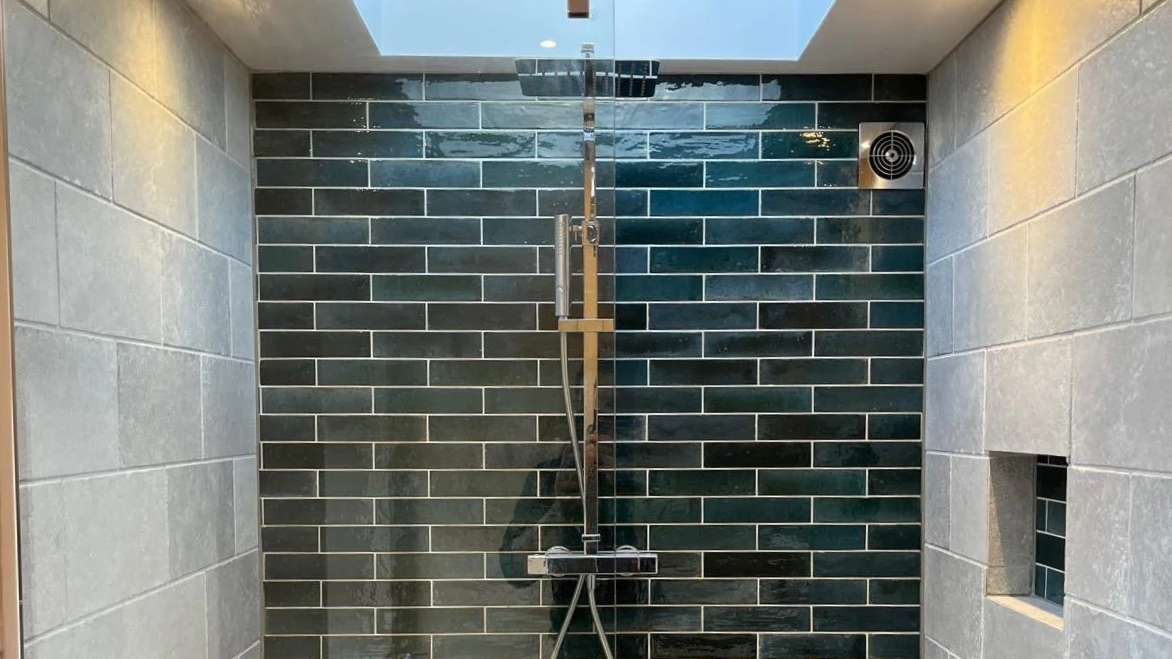 Example of our work - Modern shower with black subway tile wall, large showerhead, and a metal handle in a bathroom.