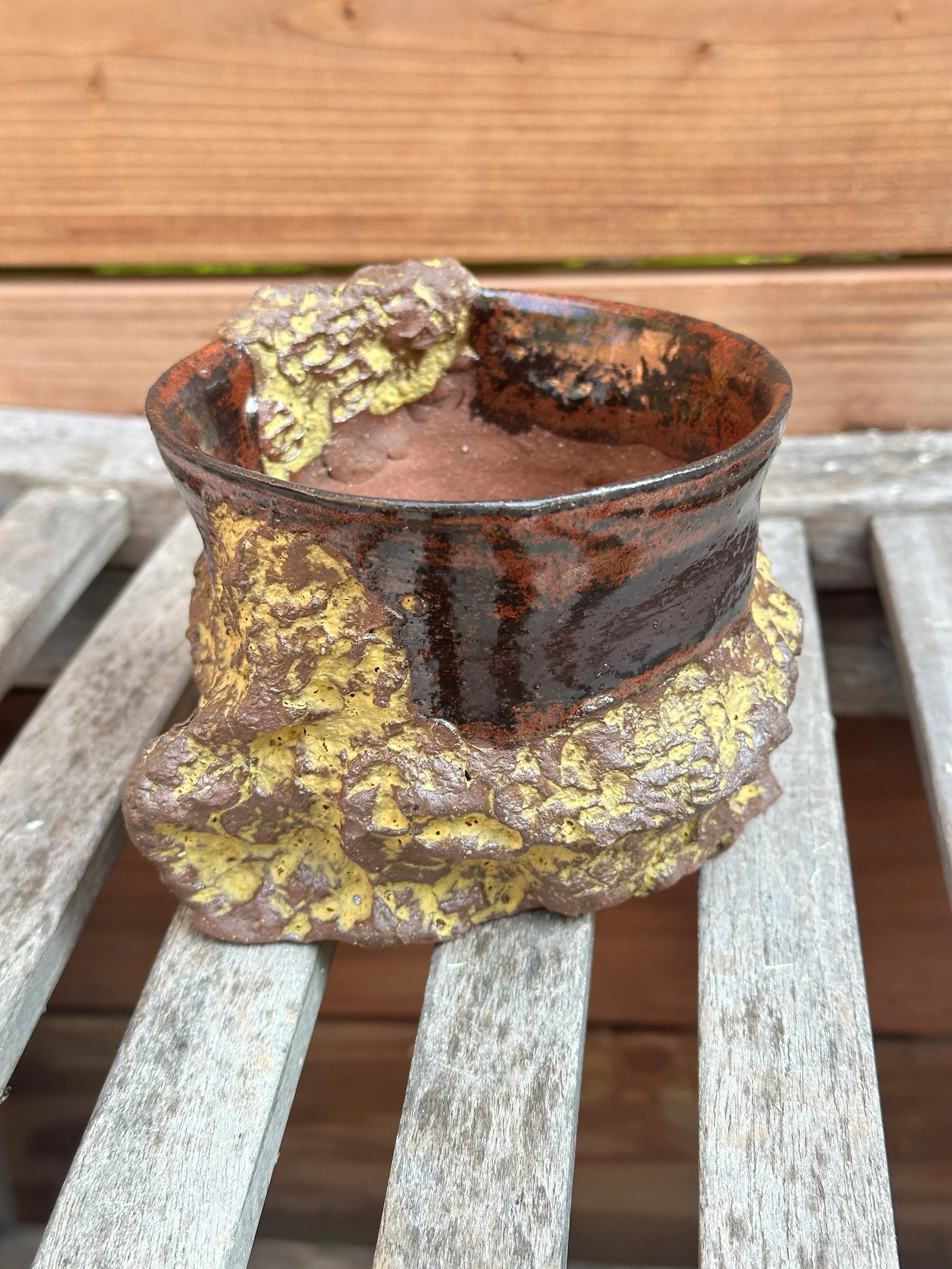Handmade ceramic pot on wooden surface with a rough, textured base and glazed upper part, against a wooden background.