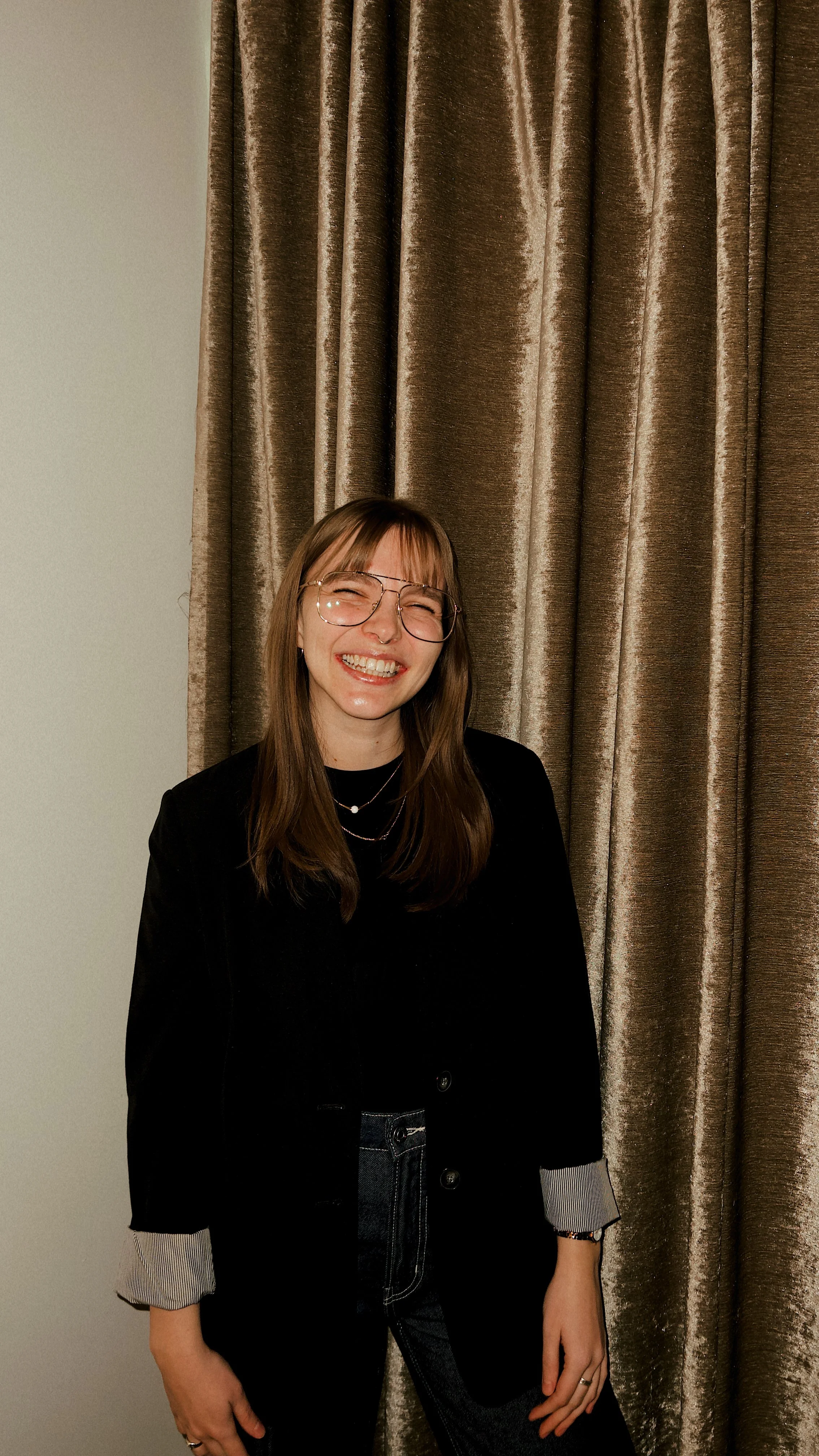 A 30-something femme with light skin and brown mid length hair with bangs smiles in front of a metallic fabric background.