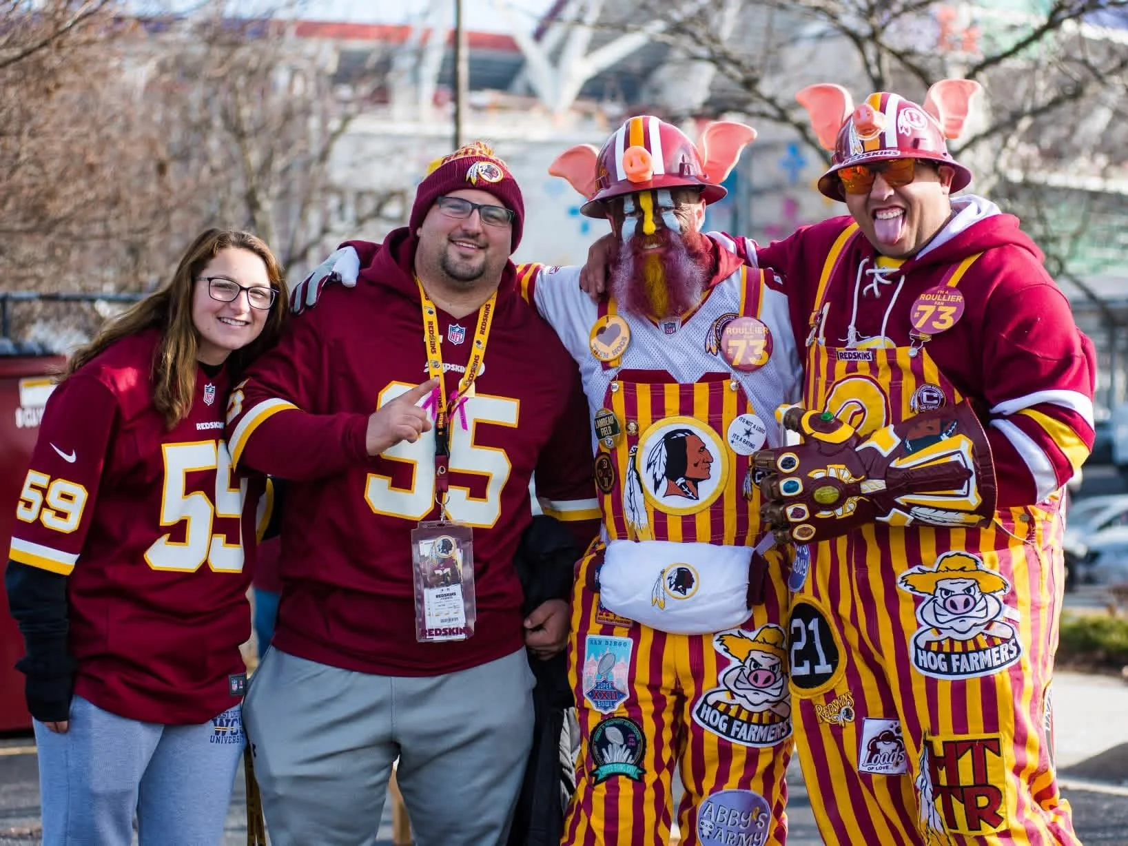 Four people standing together at an outdoor event, dressed in Washington Football Team or NFL gear, with one person wearing a pig-themed costume and accessories, smiling and posing for the camera.
