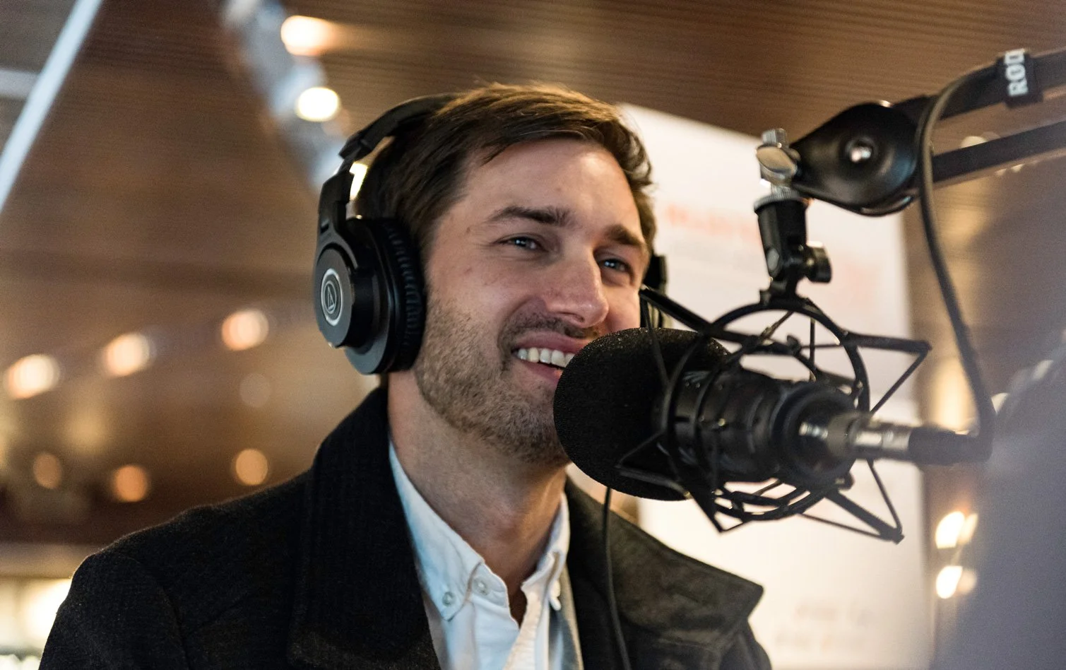 A man wearing headphones speaks into a professional microphone in a recording studio or radio station.
