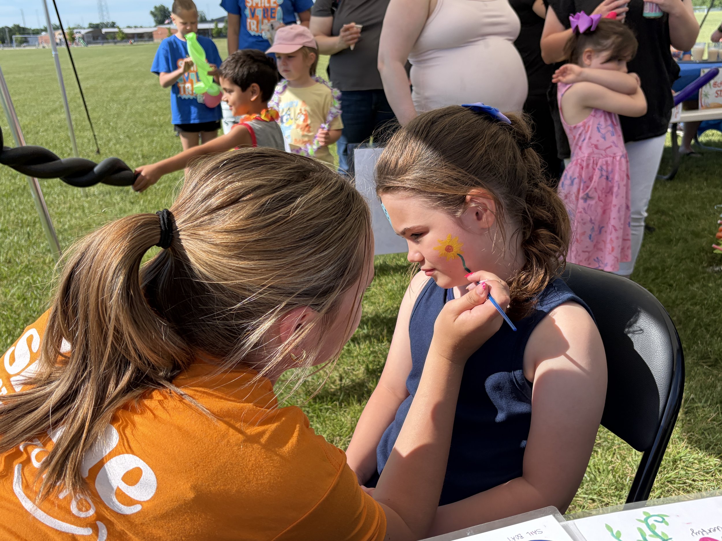Volunteer painting a child's face during the All About Kids Pediatric Dentistry Family Fun Day community event.
