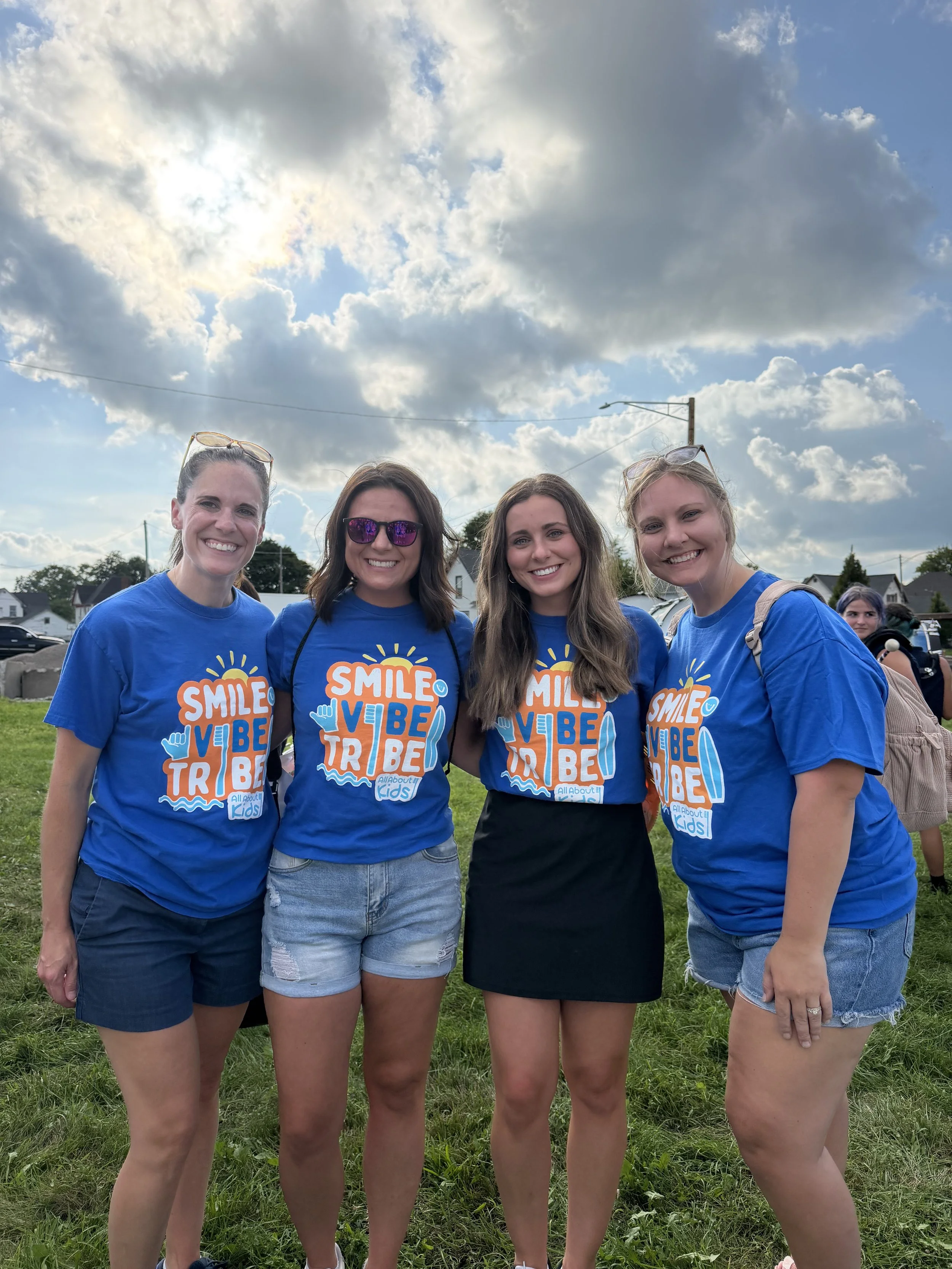 Four All About Kids Pediatric Dentistry team members smiling and wearing matching blue t-shirts at the community parade event in Napoleon.