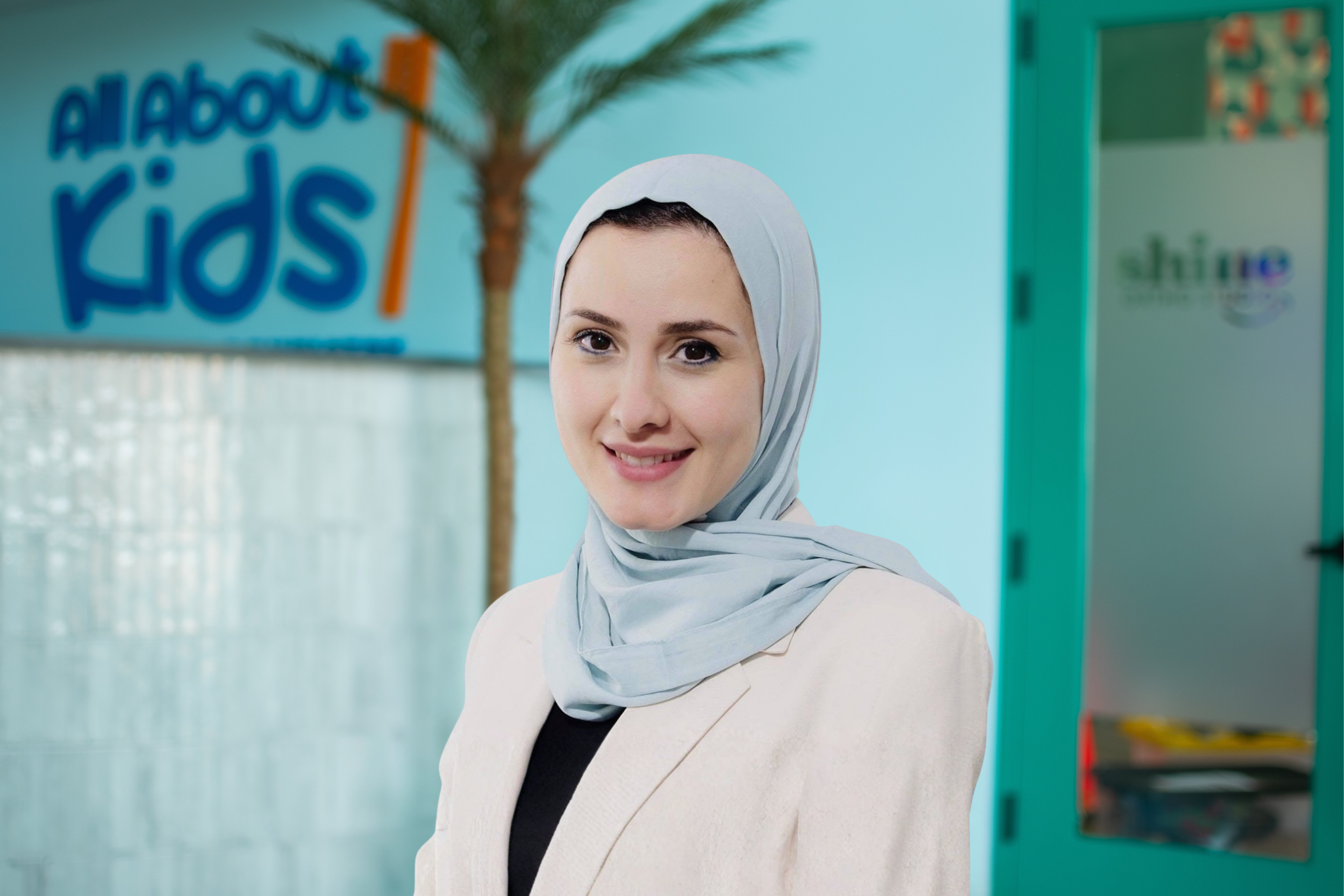 Dr. Rawan Sarsour, board certified pediatric dentist at All About Kids Pediatric Dentistry in Napoleon Ohio, standing in the office with the All About Kids logo in the background.