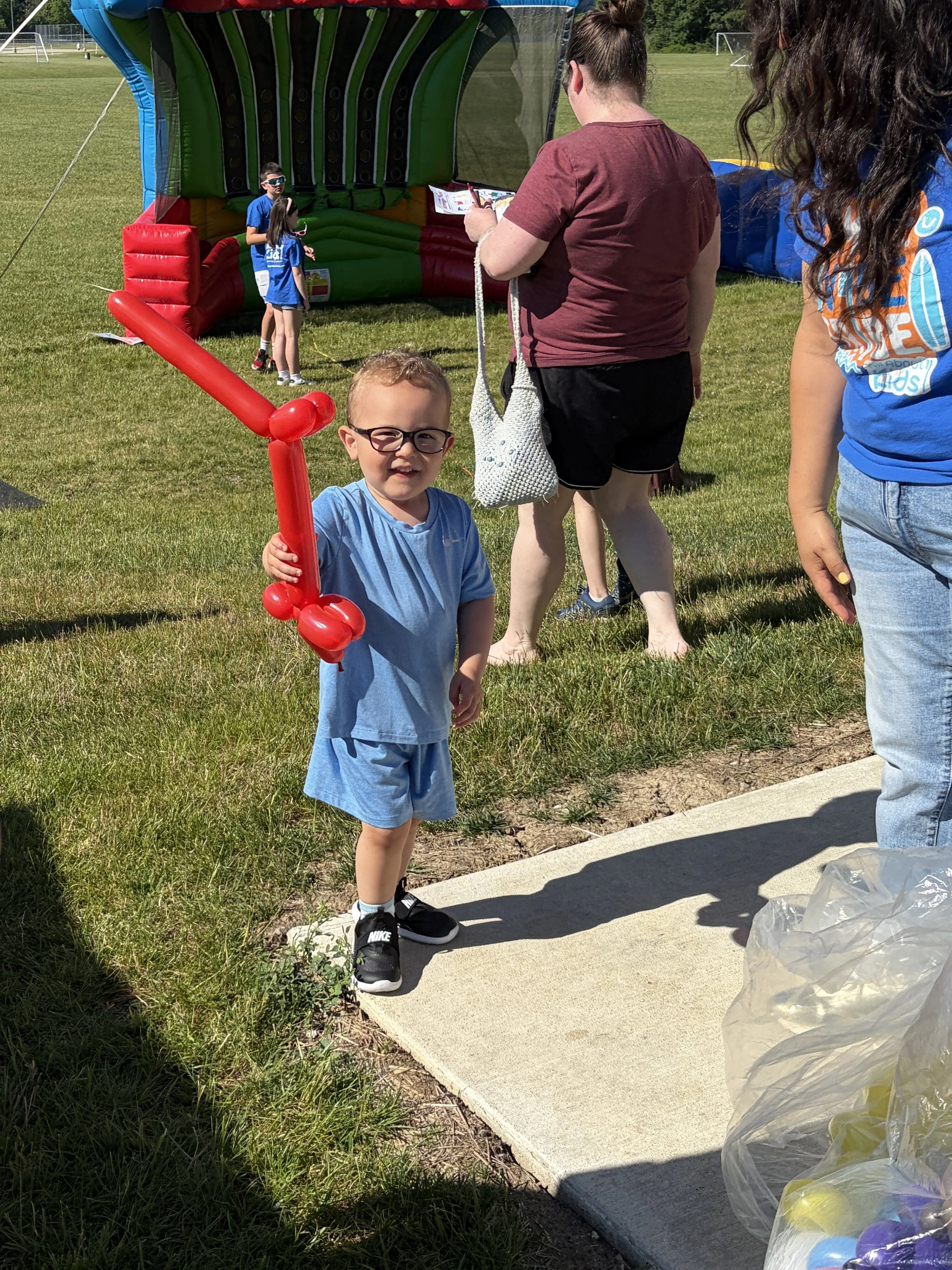 Child smiling with a balloon creation at the All About Kids Pediatric Dentistry Family Fun Day community event.