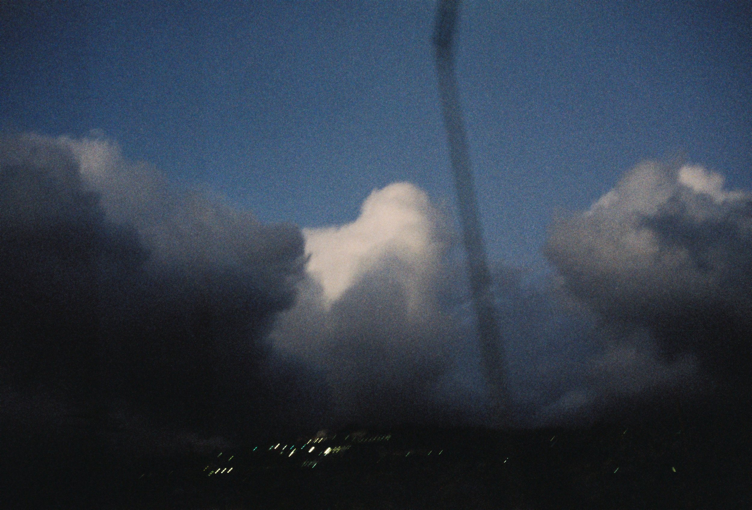 Thunderstorm with dark clouds and a visible lightning bolt in the sky at night, city lights below.