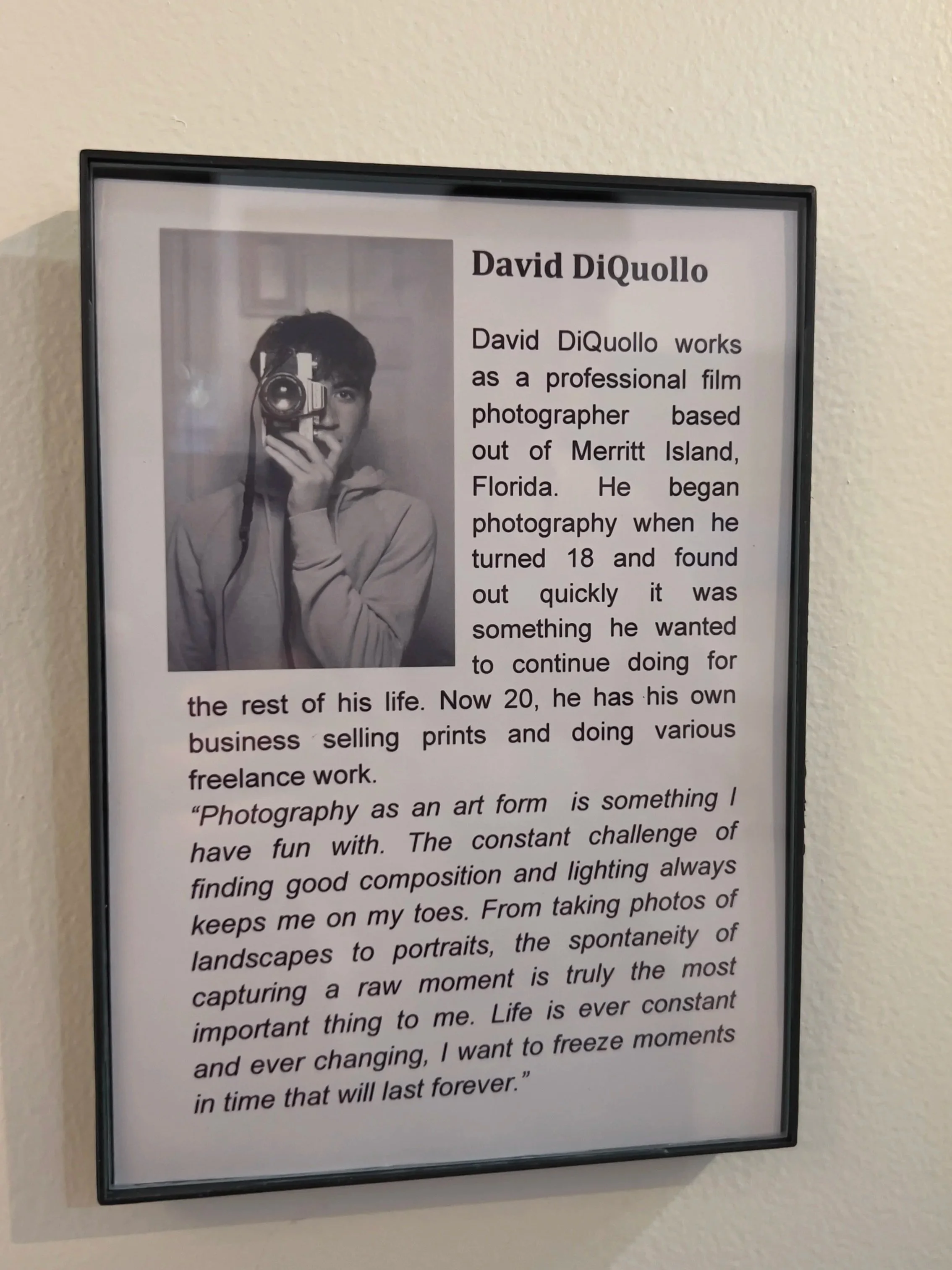 Black and white photo of a young man holding a camera to his face, taking a picture, with only his eyes visible.