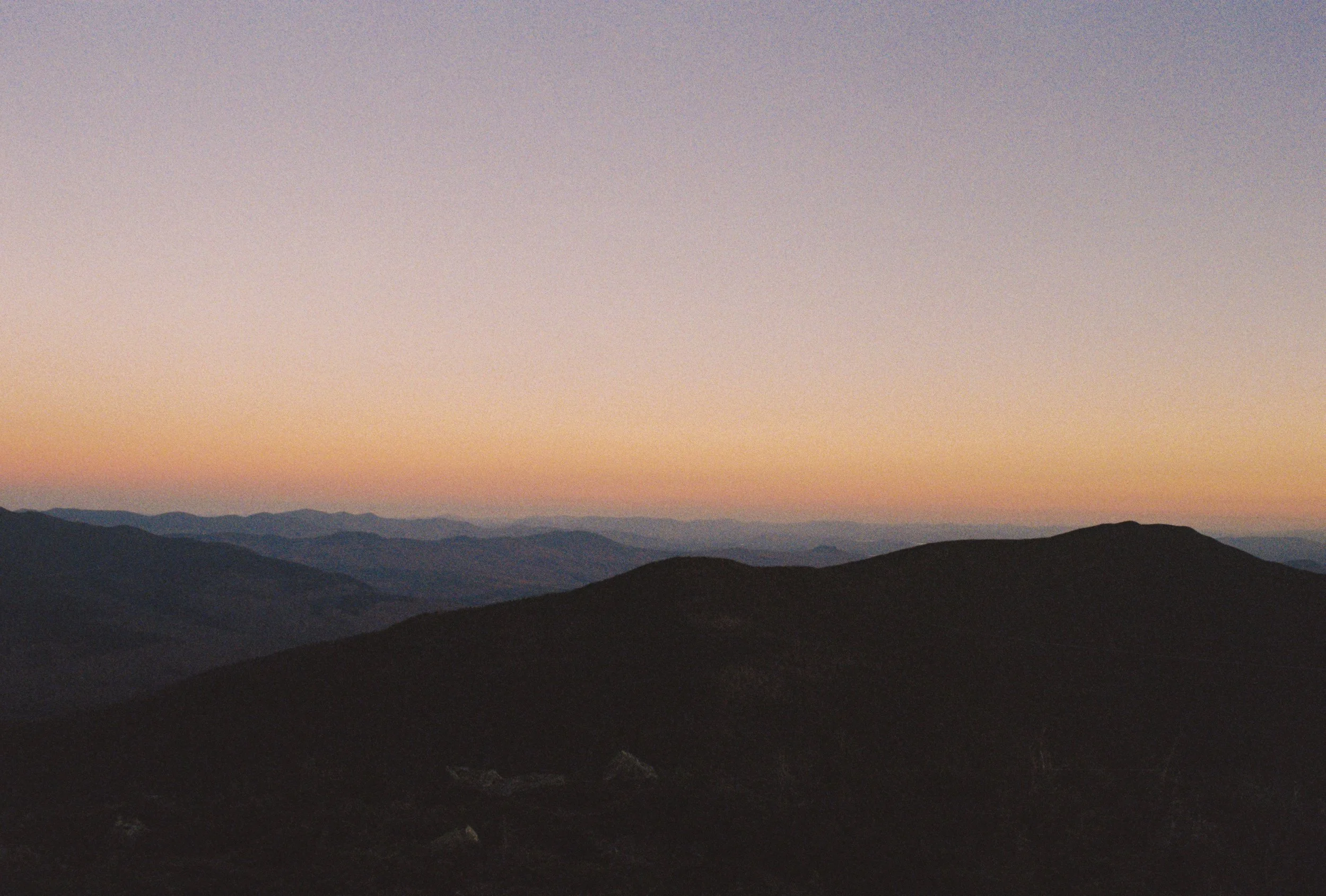 Sunset or sunrise over a mountain range with a gradient sky in soft pastel colors.