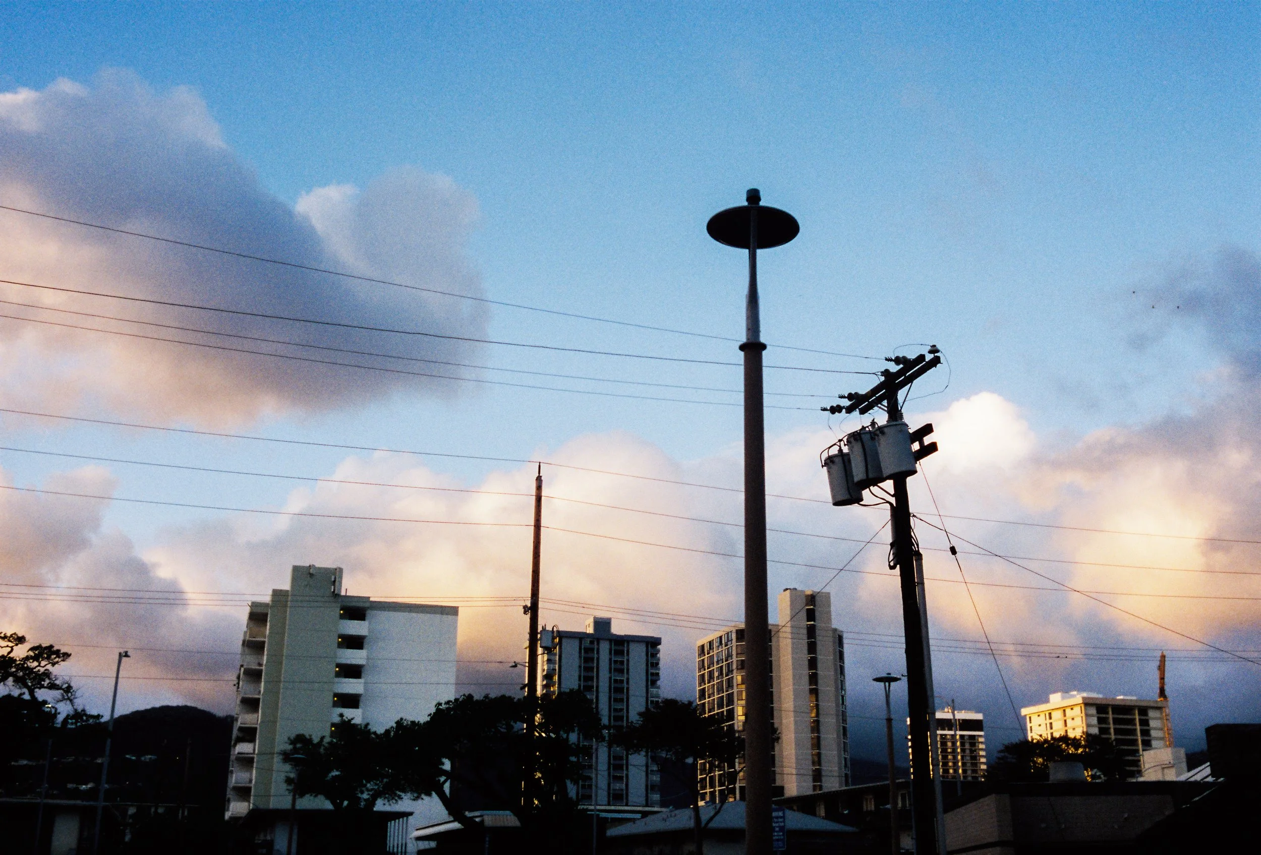 A cityscape during sunset with high-rise buildings, a utility pole, and clouds in the sky.