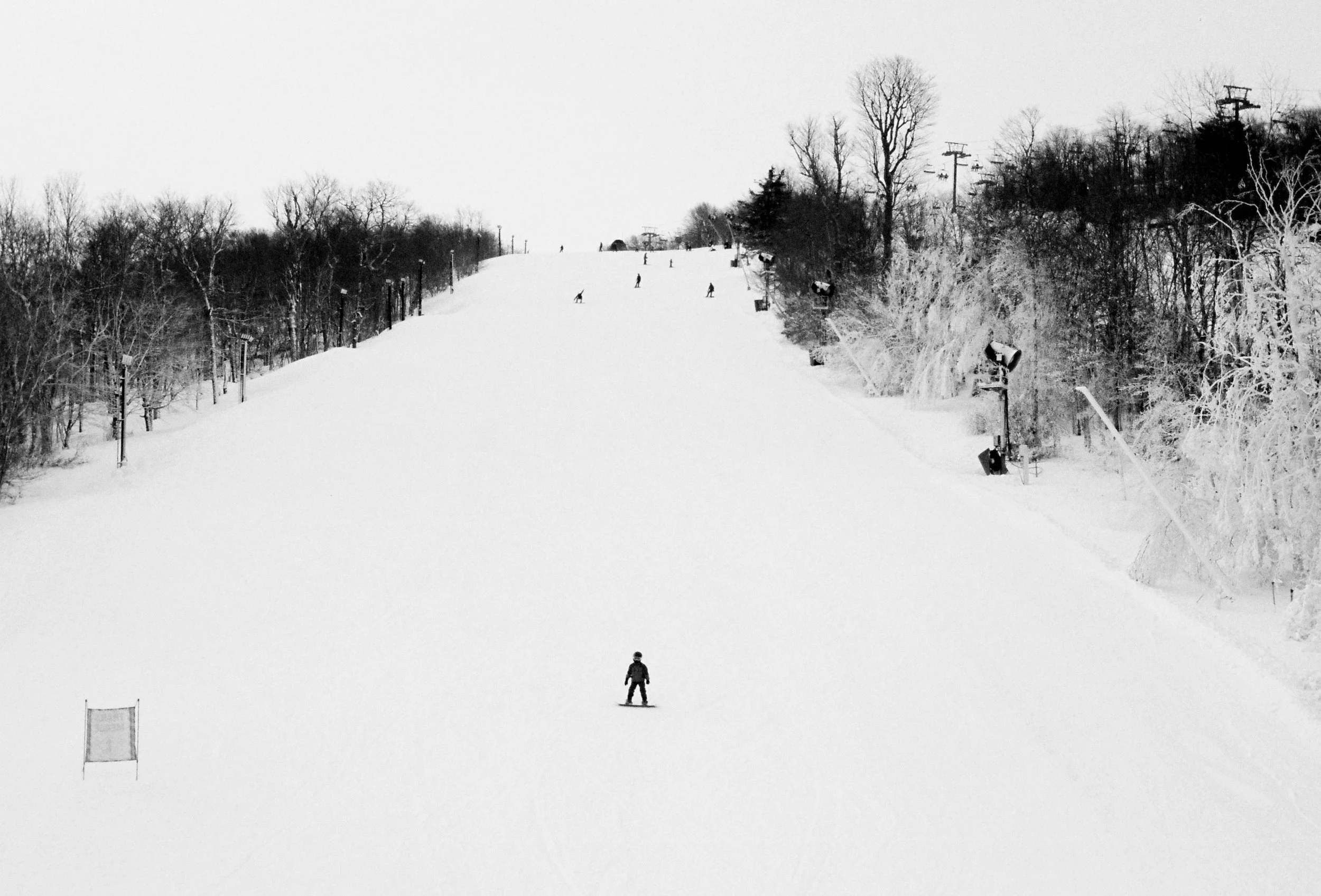 A skier on a snowy ski slope with trees and ski lift poles in the background.