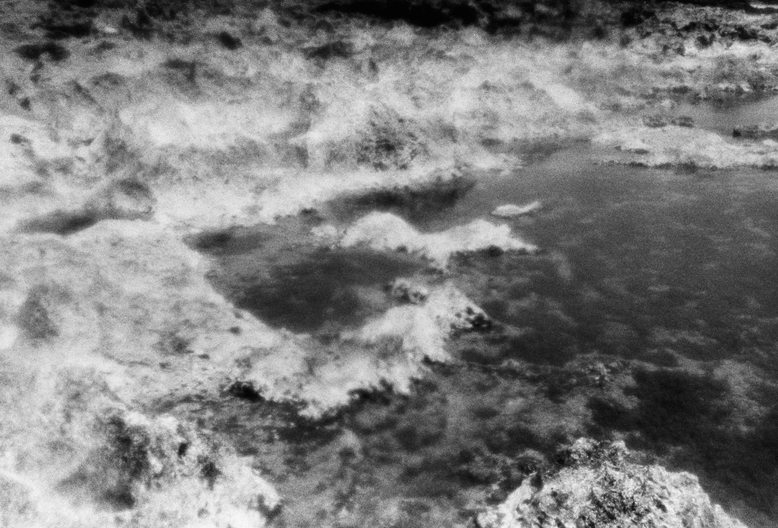 Black and white photograph of a dry rock formation in Hawaii and a tidal bay of water.