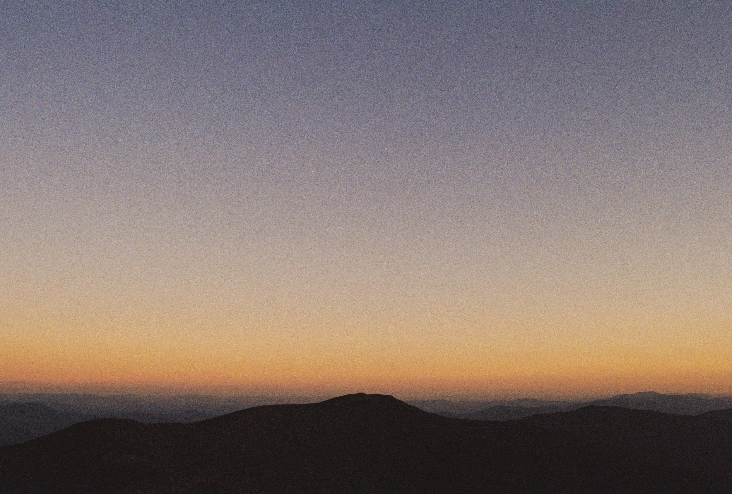 Sunset over mountain range with gradient sky changing from orange to dark blue.